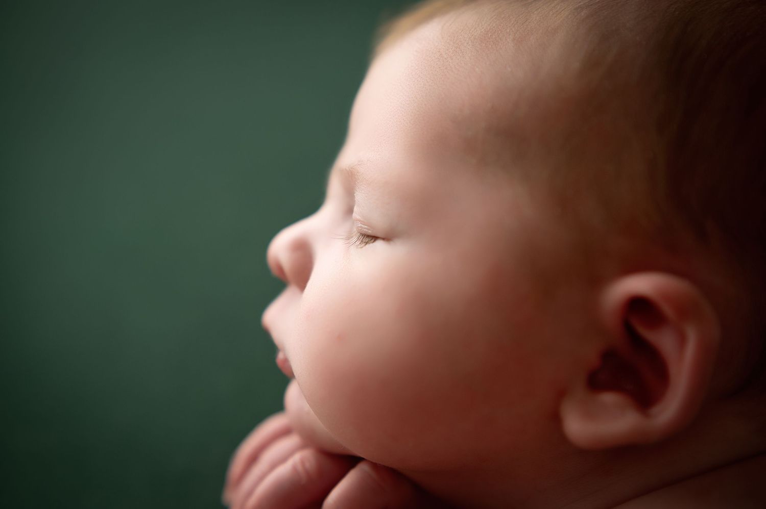 Close-up profile of sleeping newborn against dark green background.