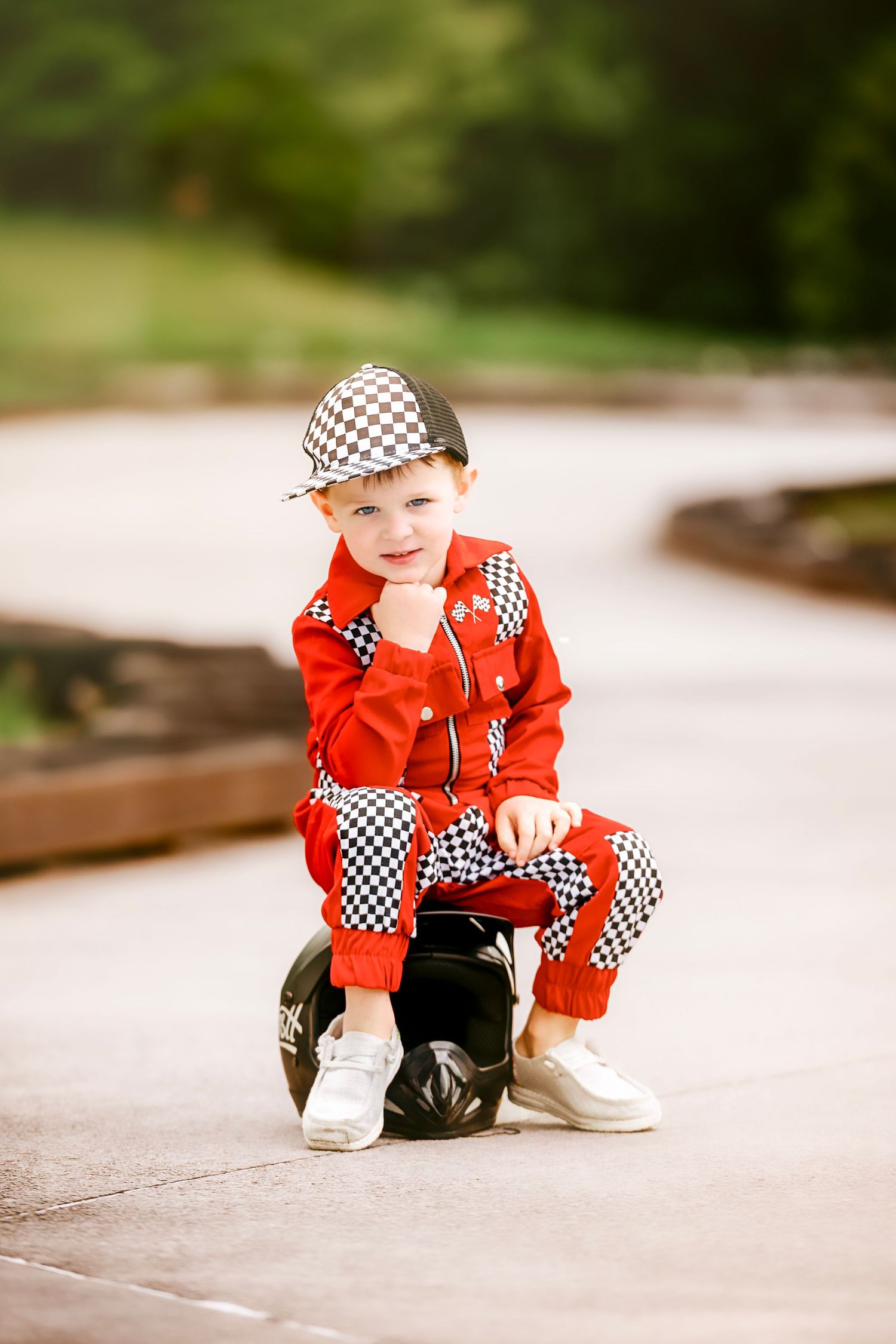 Child in red racing outfit with checkered pattern crawls on concrete surface.