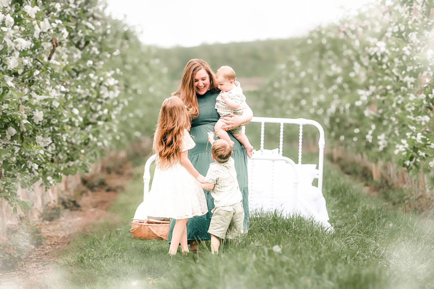 Family portrait in spring orchard with white iron bed frame among blooming trees.