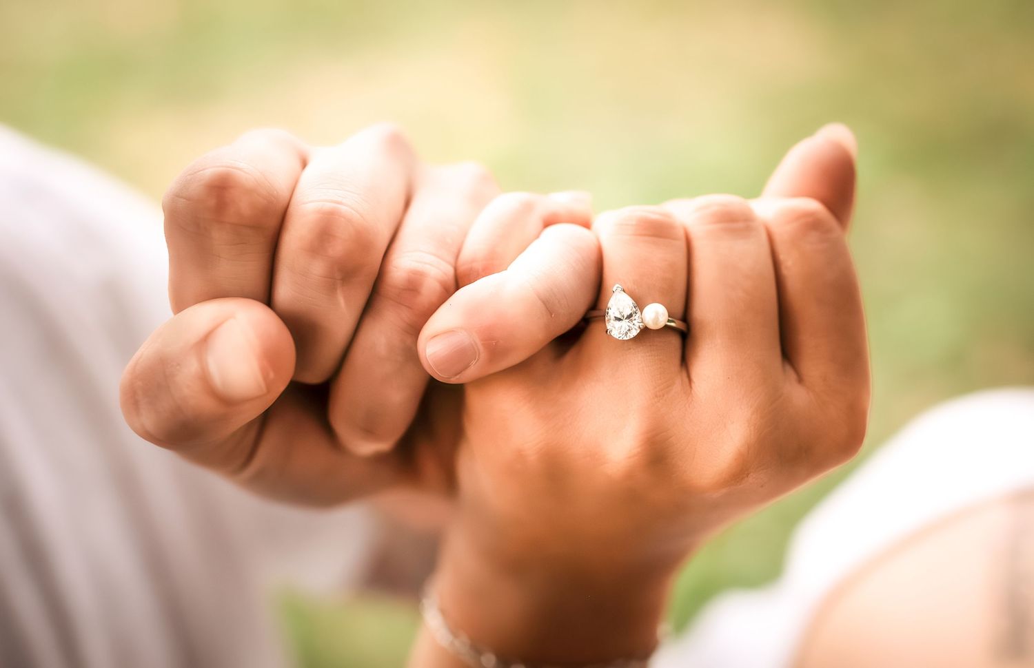 Close-up of hands showing engagement ring in natural outdoor lighting.