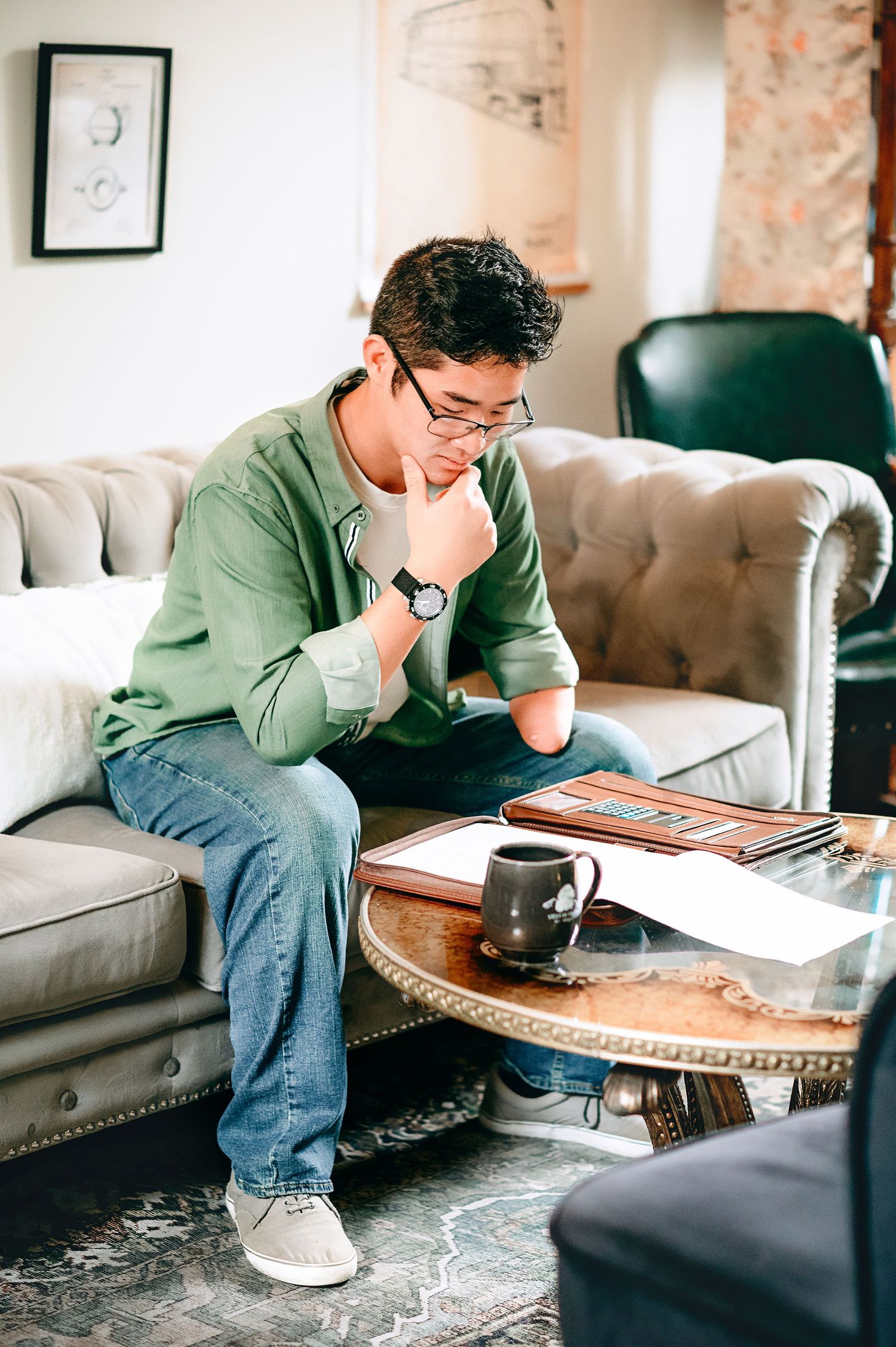 Person in casual attire studies at coffee table with books and hot beverage.