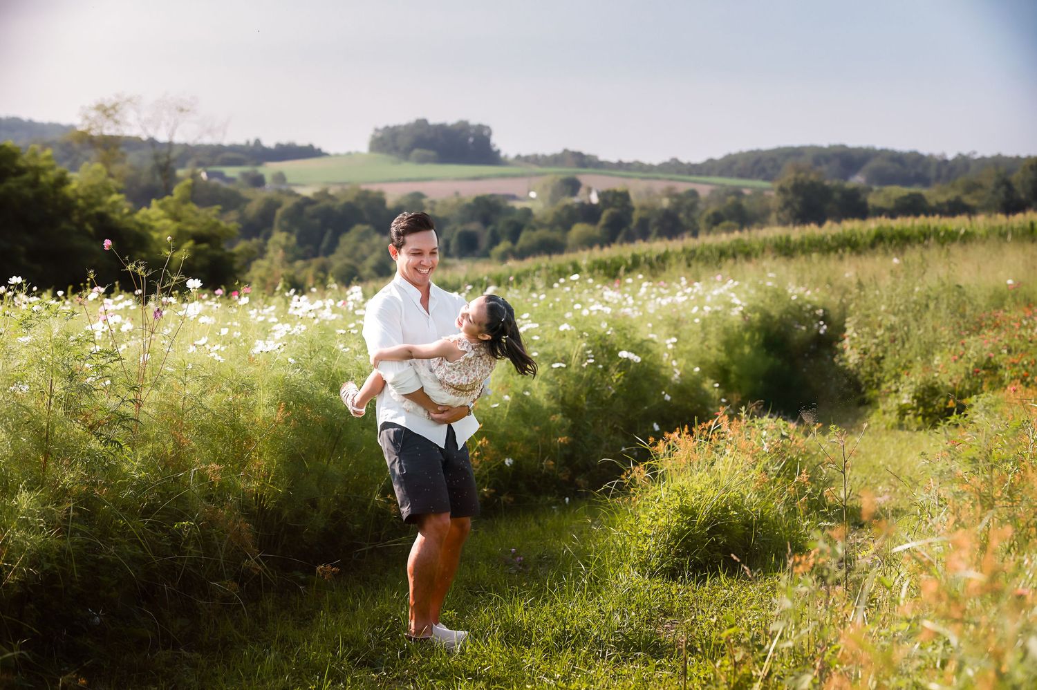 A couple embraces in a sunlit meadow filled with wildflowers during a romantic outdoor photoshoot.