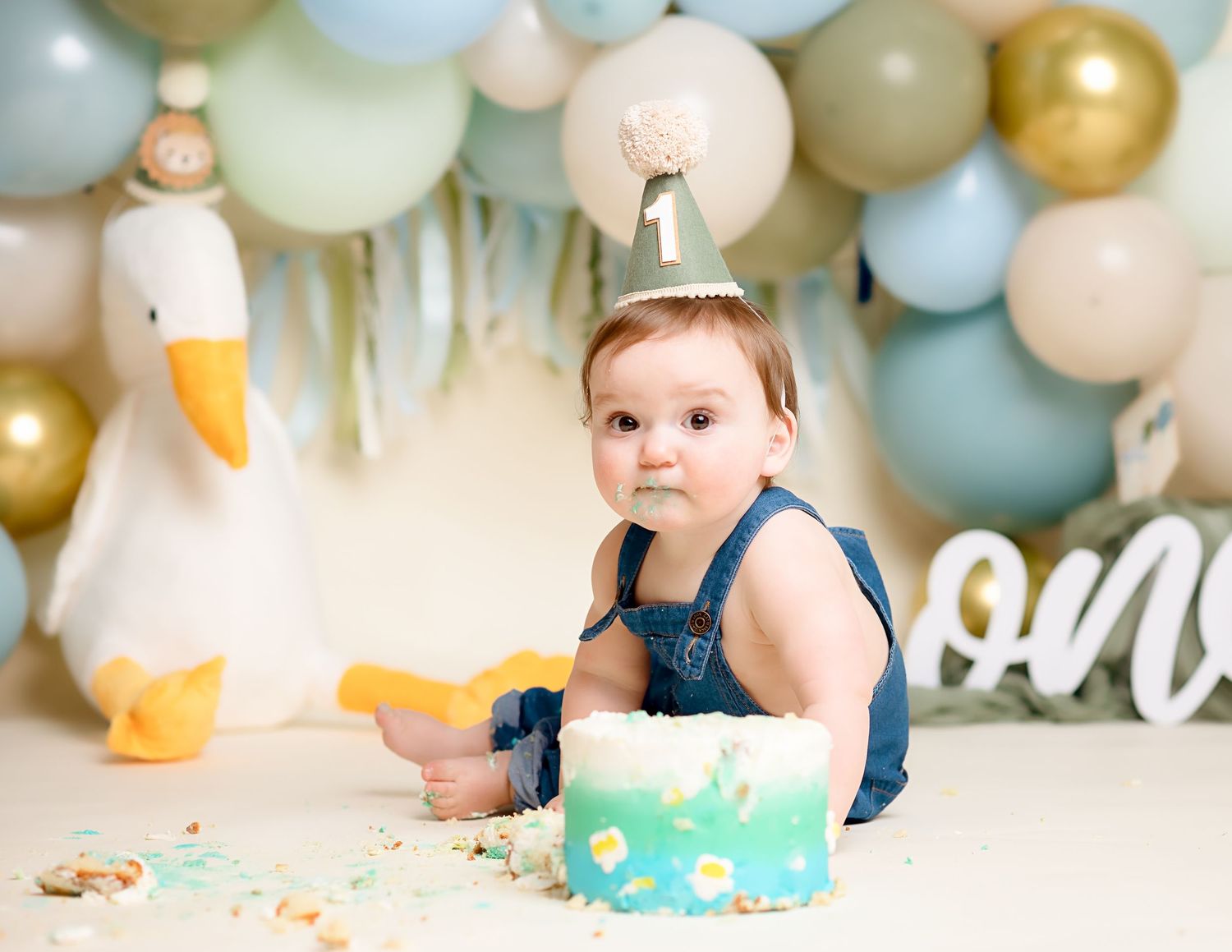 First birthday party setup with gold and pastel balloon decorations against a white backdrop.