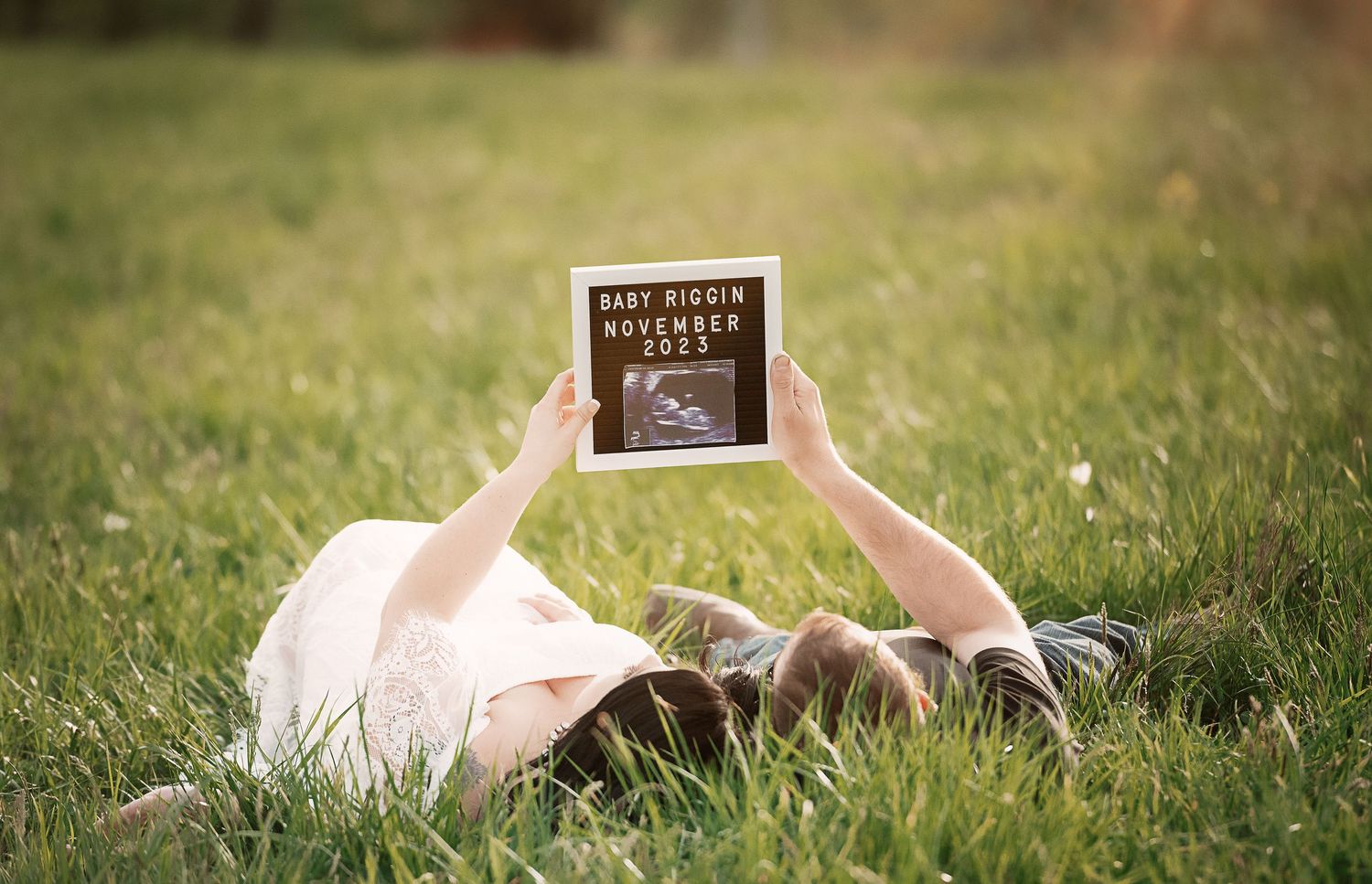 Person lying in grass holding up a book against blue sky.