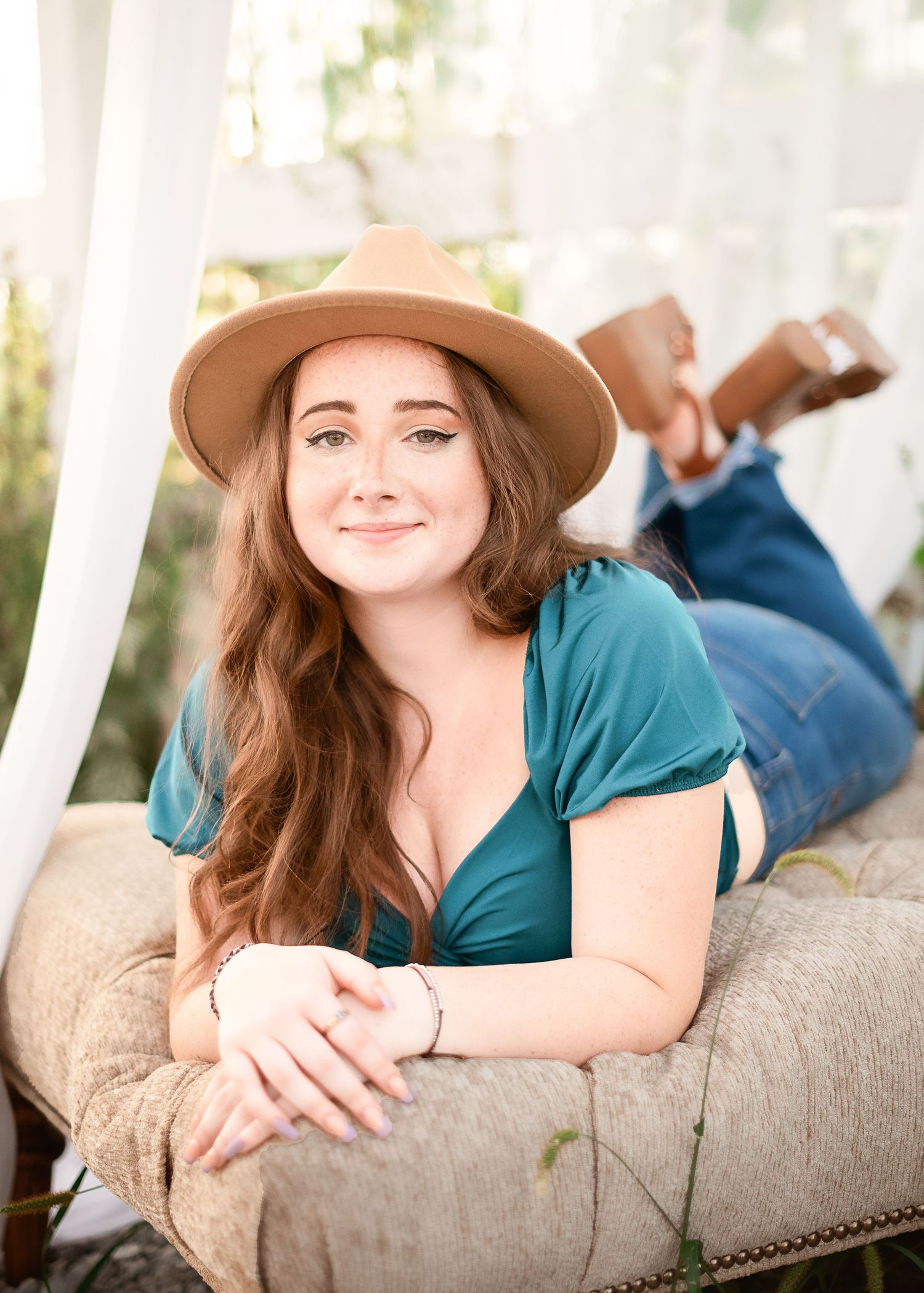 Casual portraits on a beige couch wearing a teal top and brown hat.