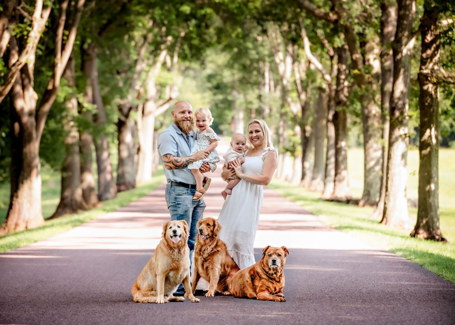 Family and their golden retriever posing together on a tree-lined path.