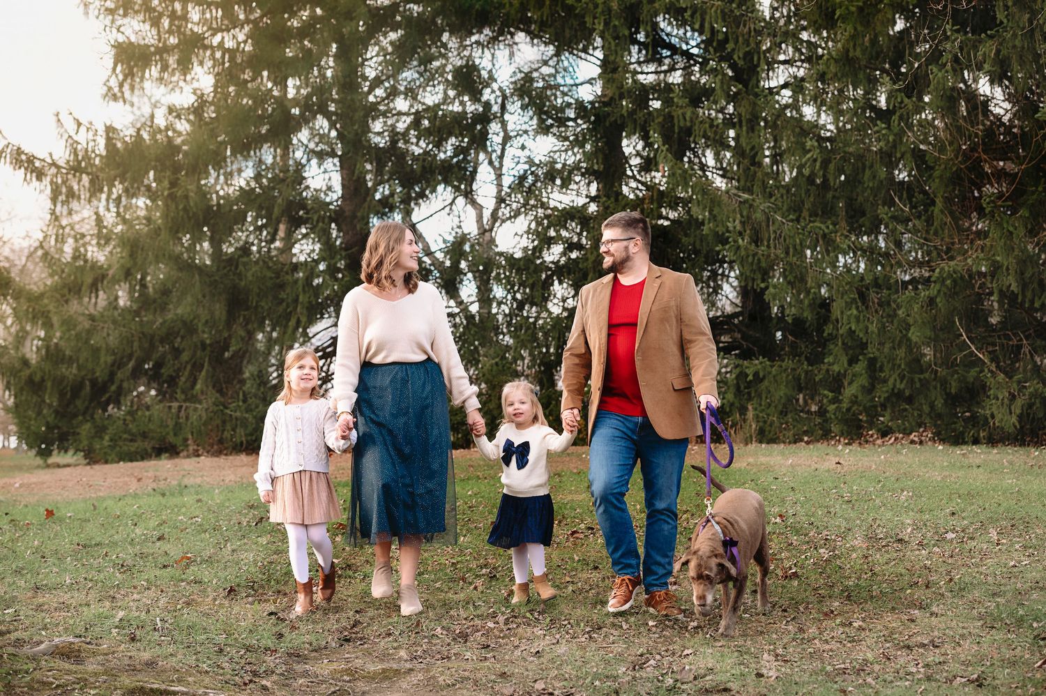 A group walks together on a grassy path beneath tall trees during golden hour.