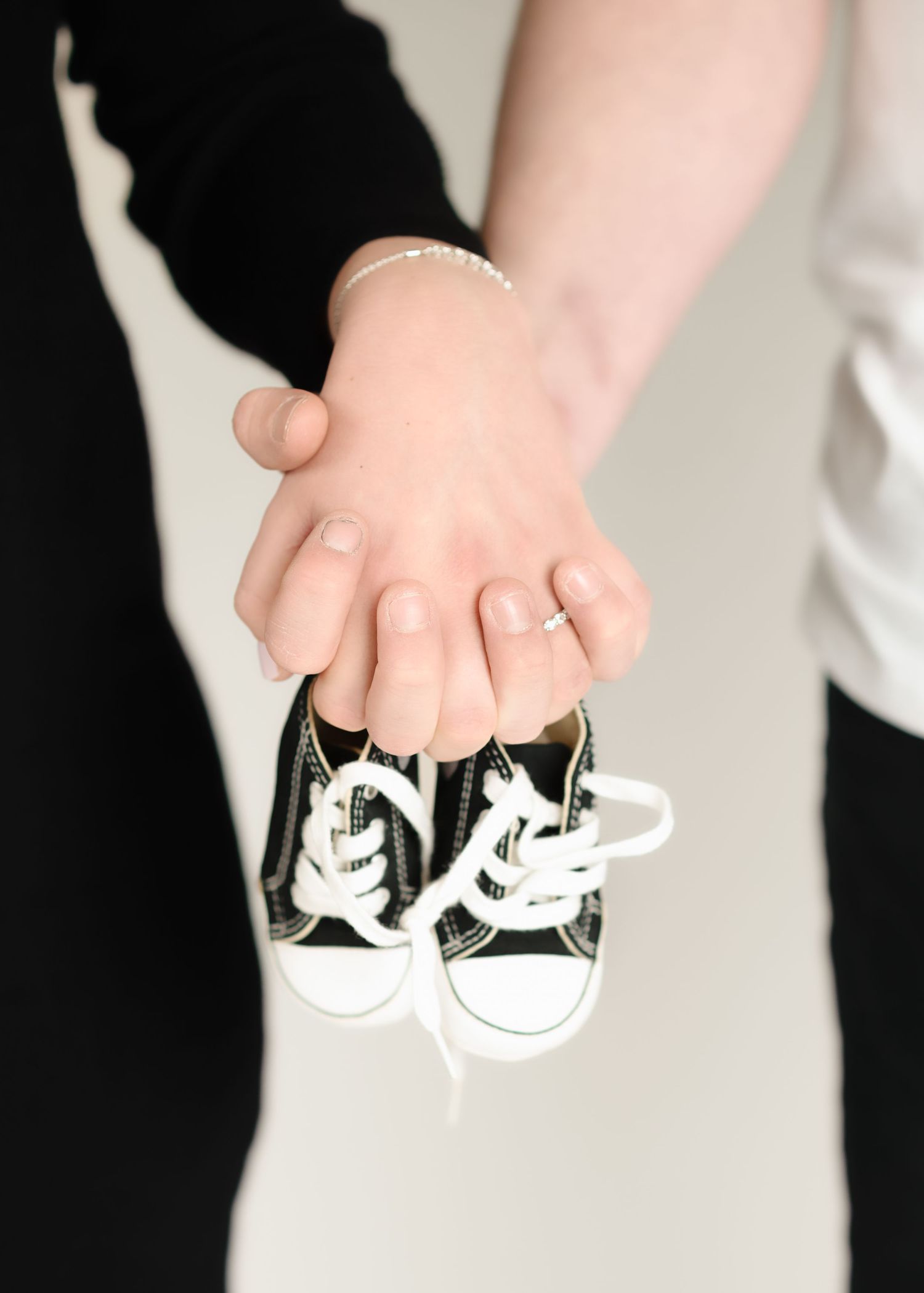 Small black and white baby shoes held against light background in maternity photo.