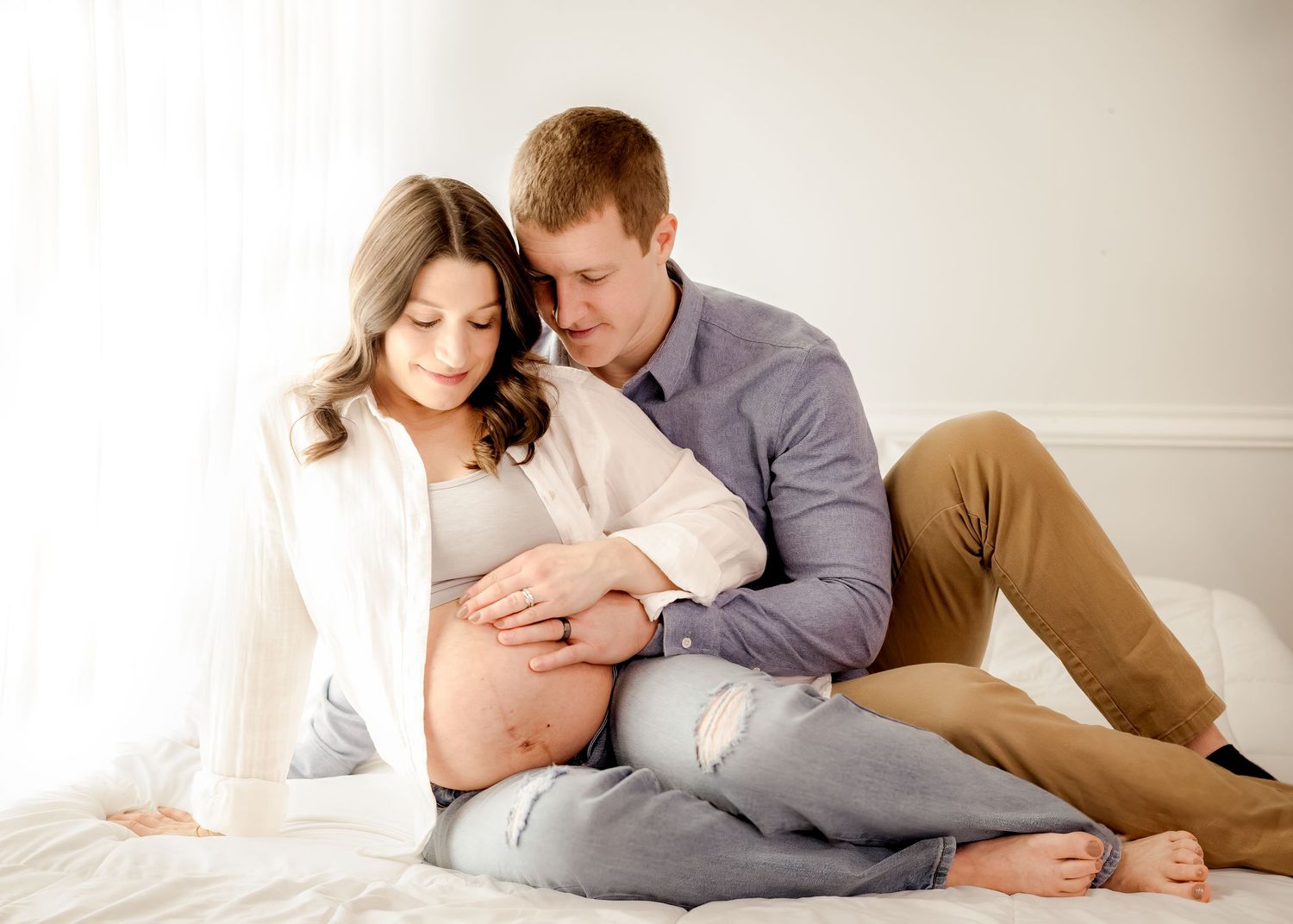 Intimate lifestyle maternity session with couple lounging in soft natural light.