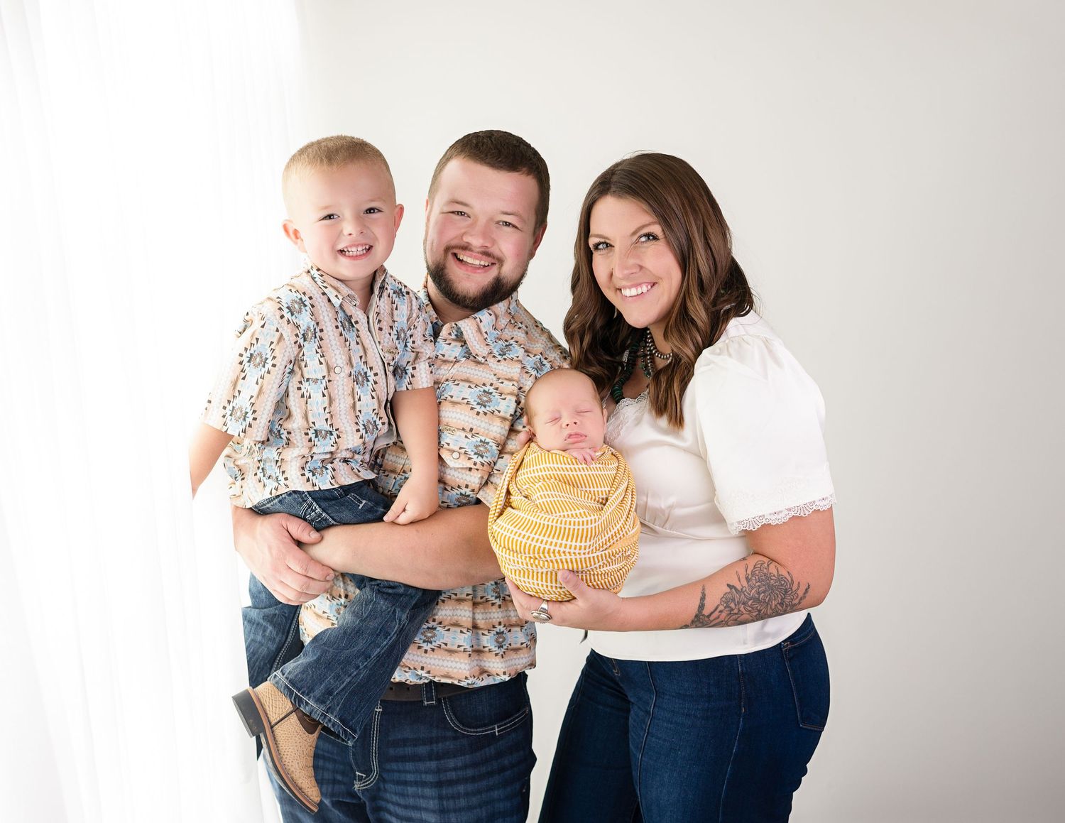 Happy family of four posing together in coordinated neutral outfits against white background.