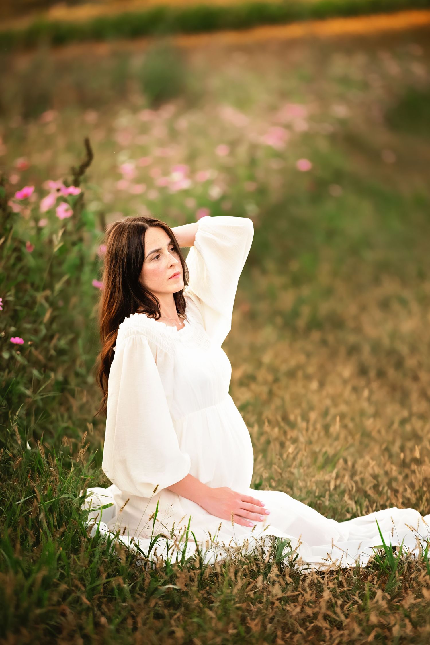 A woman in flowing white dress poses gracefully in a field of pink wildflowers.