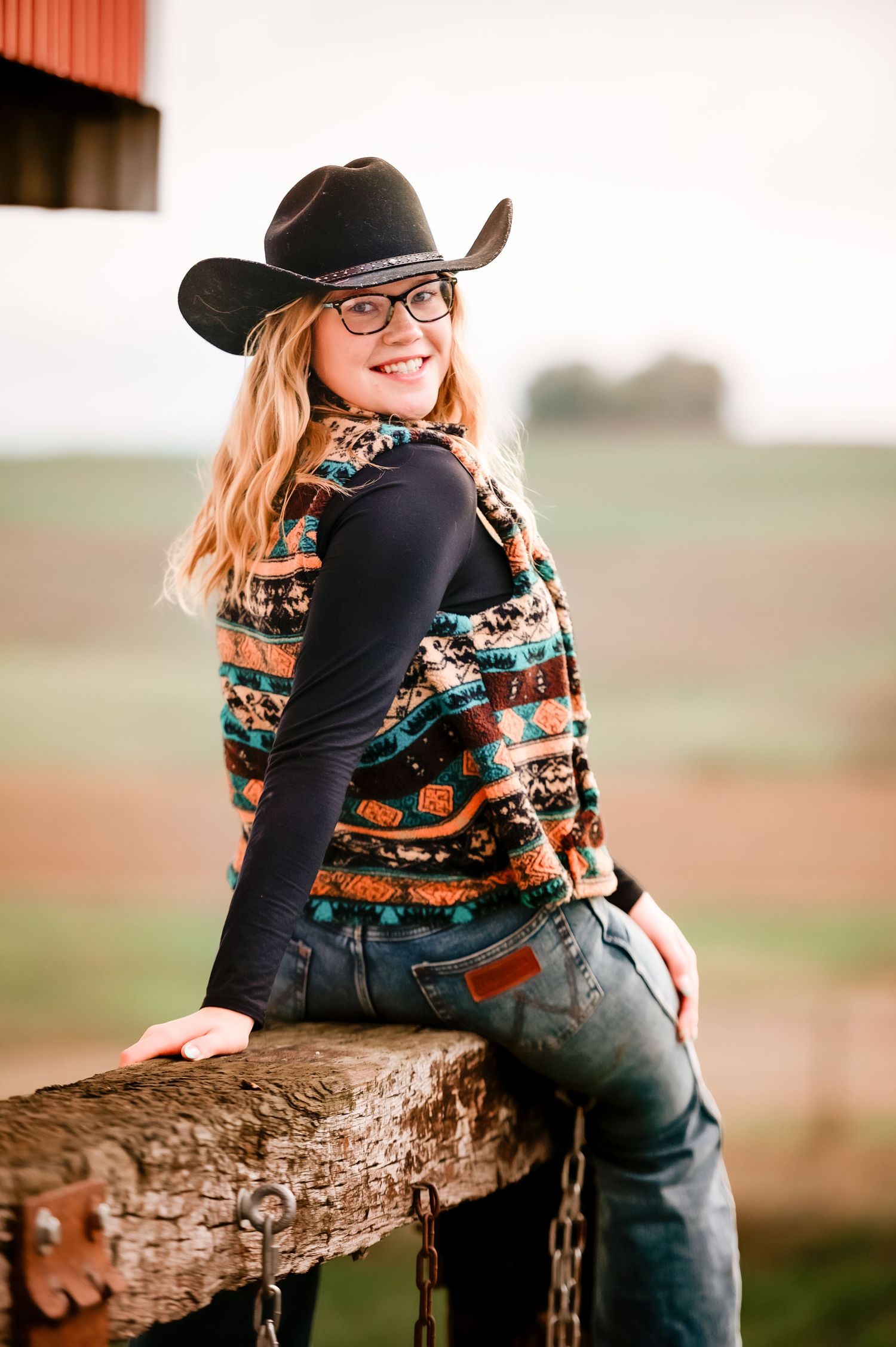 Casual western-themed photo shoot with a cowboy hat and decorative sweater on a rustic wooden fence.