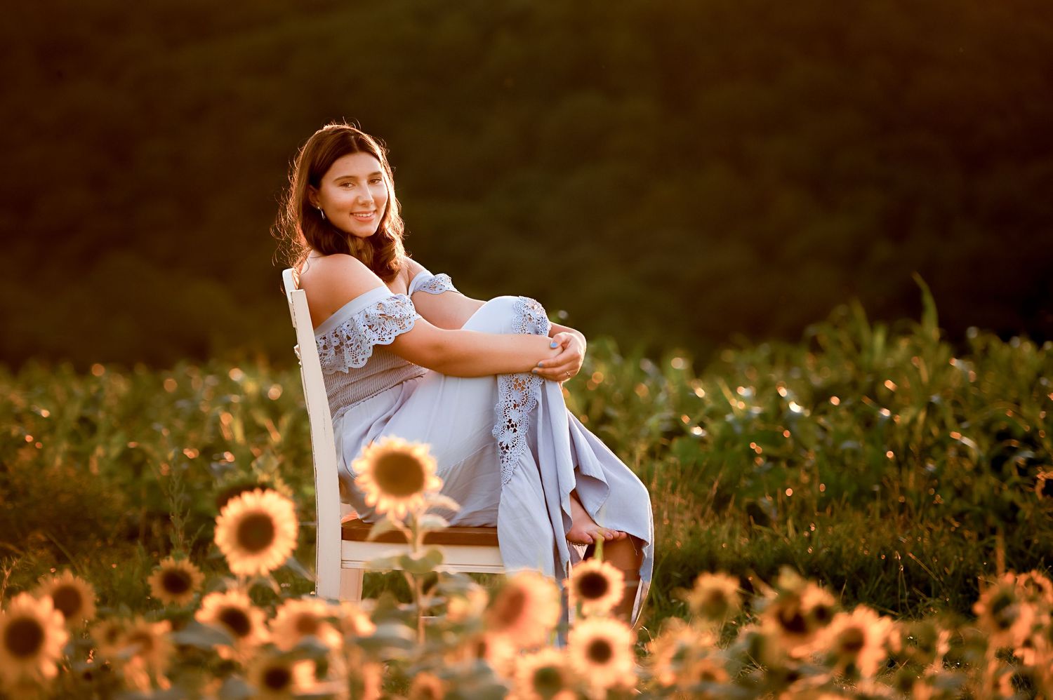 Dreamy portrait in a sunflower field wearing a light blue dress at golden hour.