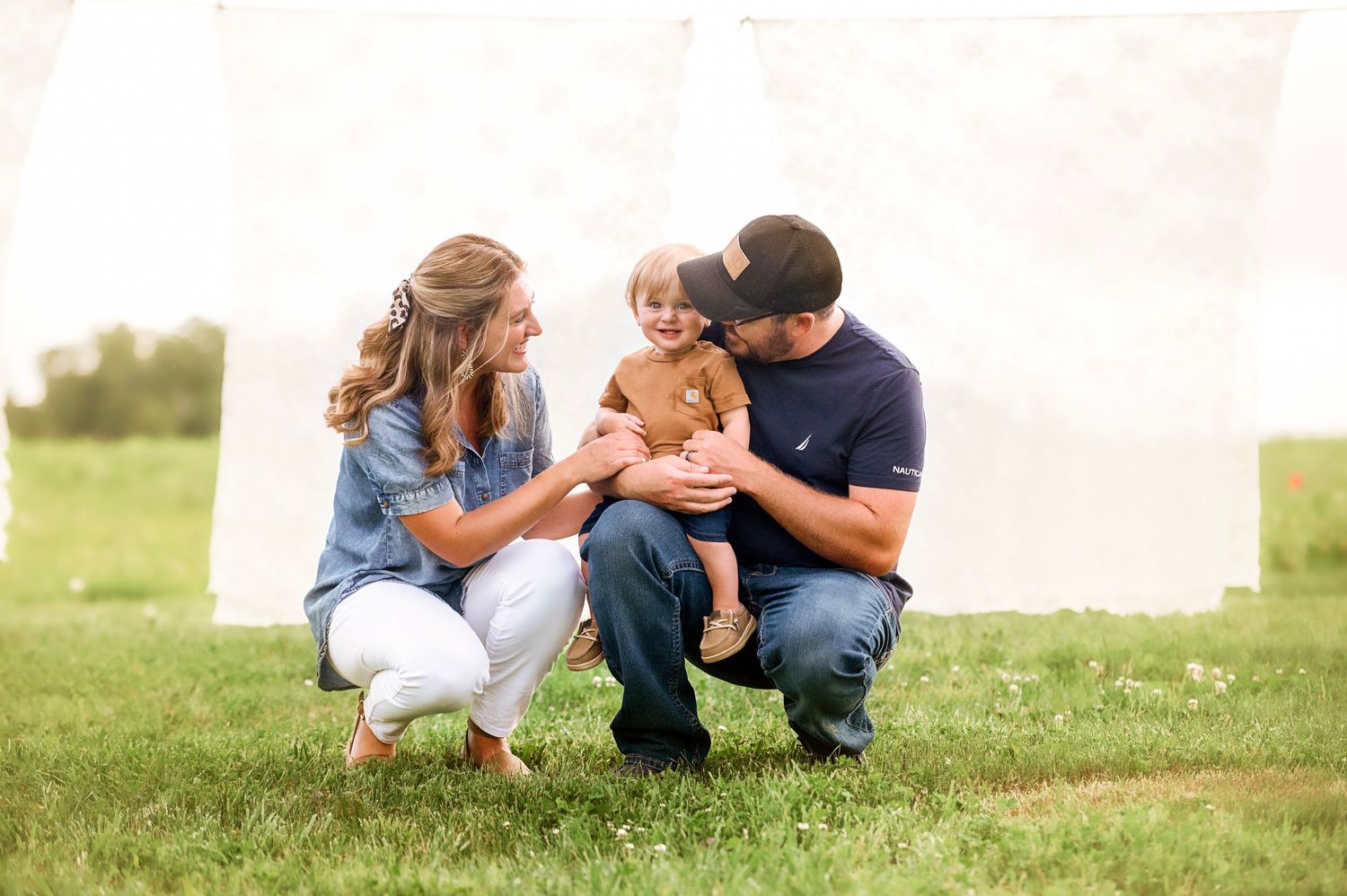 Family shares intimate moments together on a grassy hillside during a summer day.