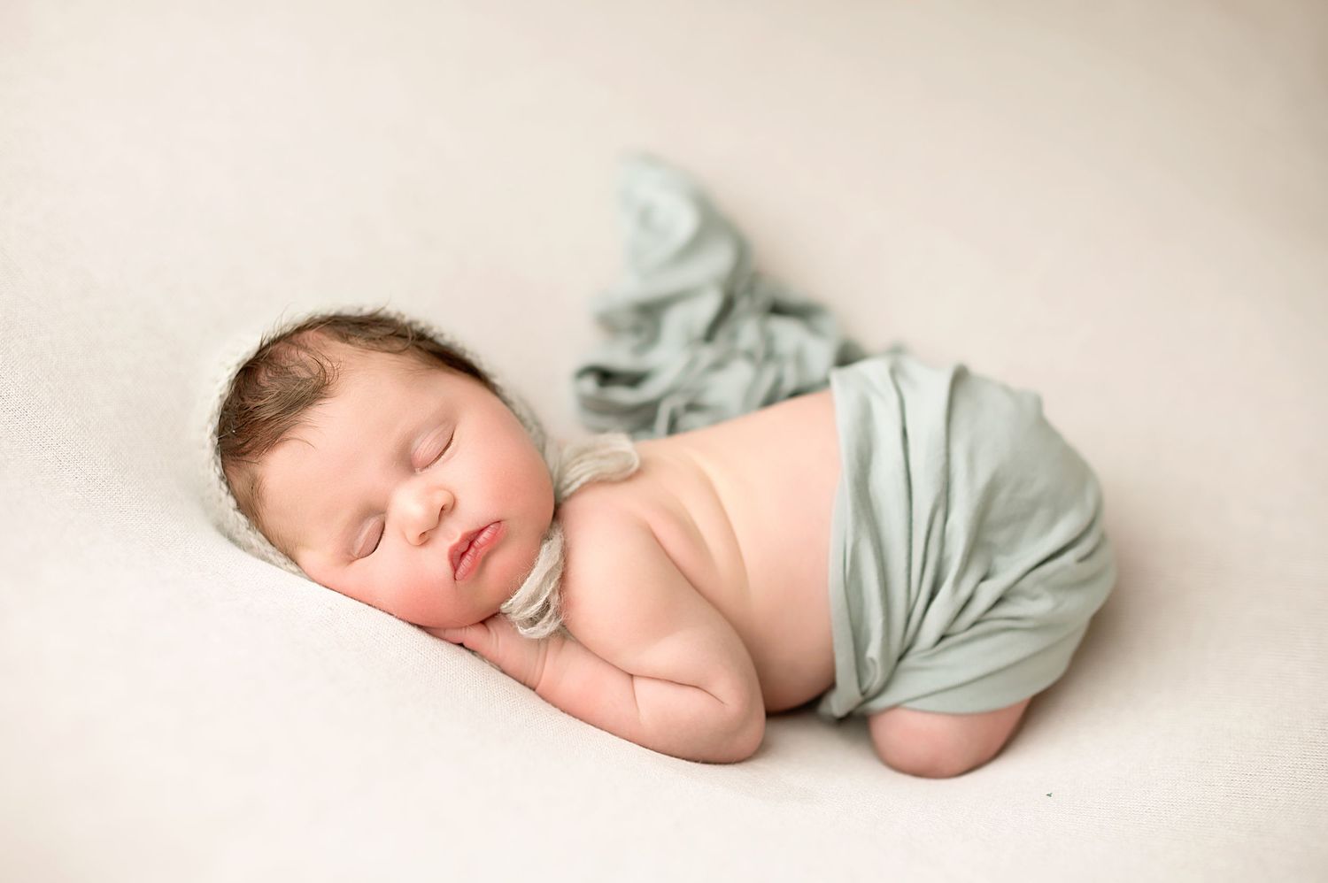 Sleeping newborn in soft blue wrap photographed in gentle natural light.