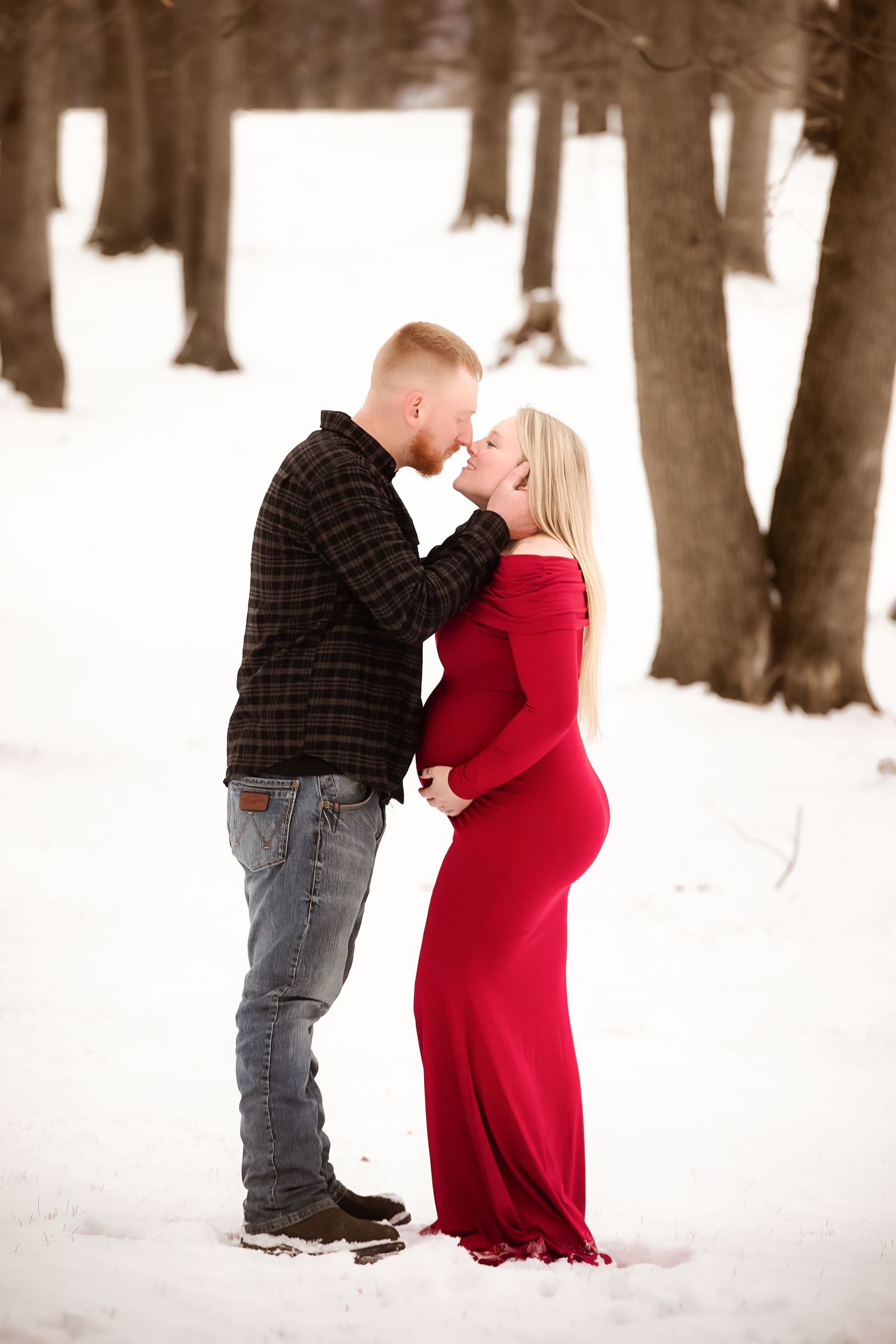 A winter engagement photo session in a snow-covered forest with tall bare trees.