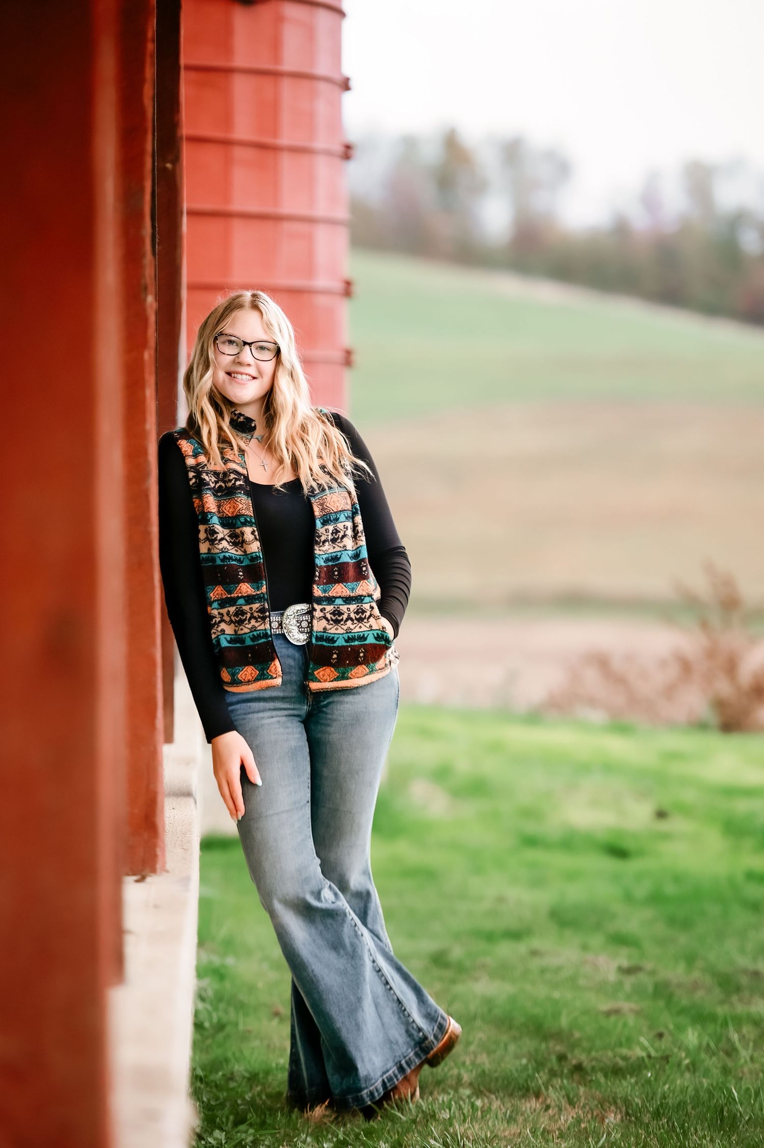 Country style portrait session featuring a patterned sweater and jeans against a rustic red barn backdrop.