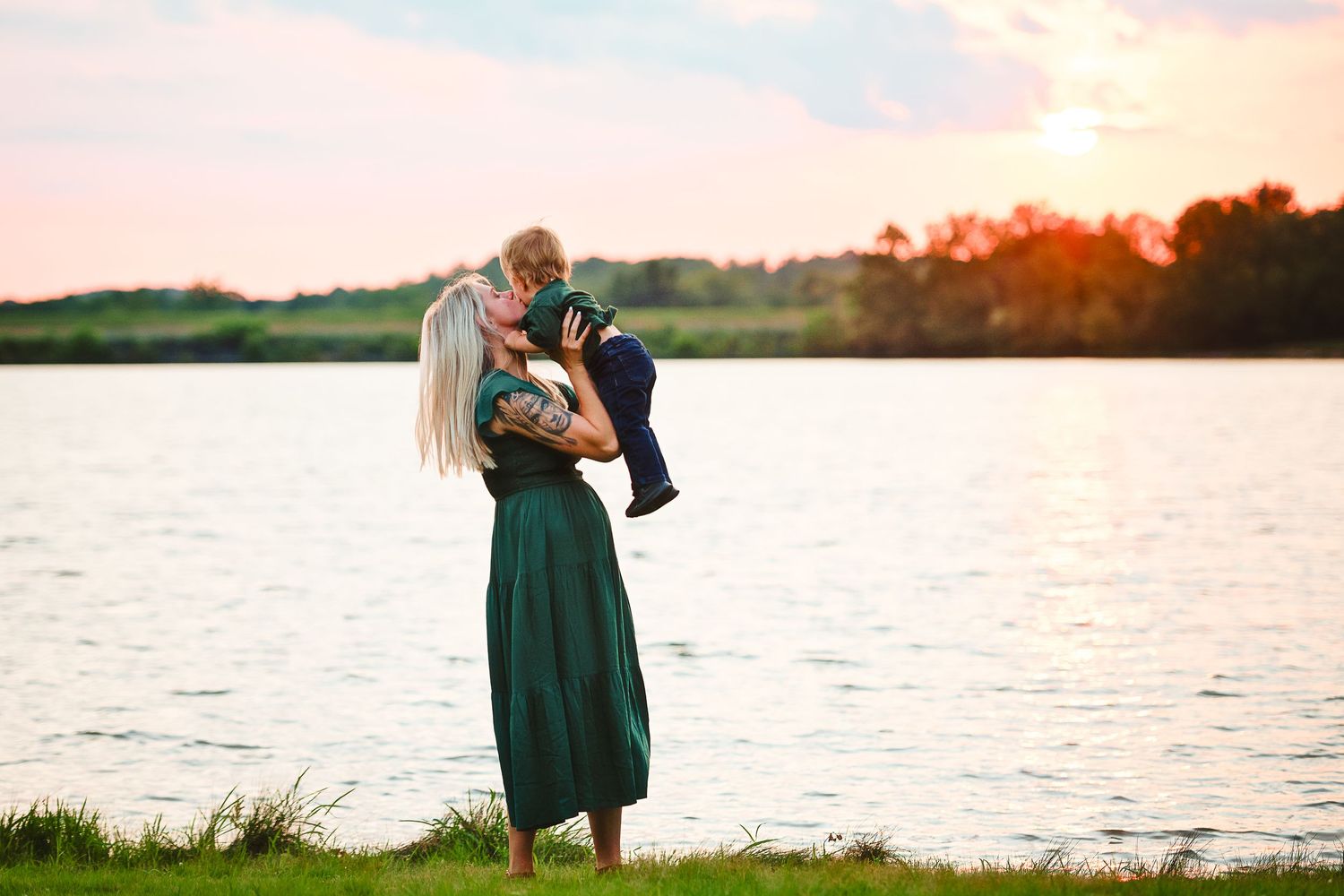 Couple embracing by a tranquil lake during golden hour sunset.