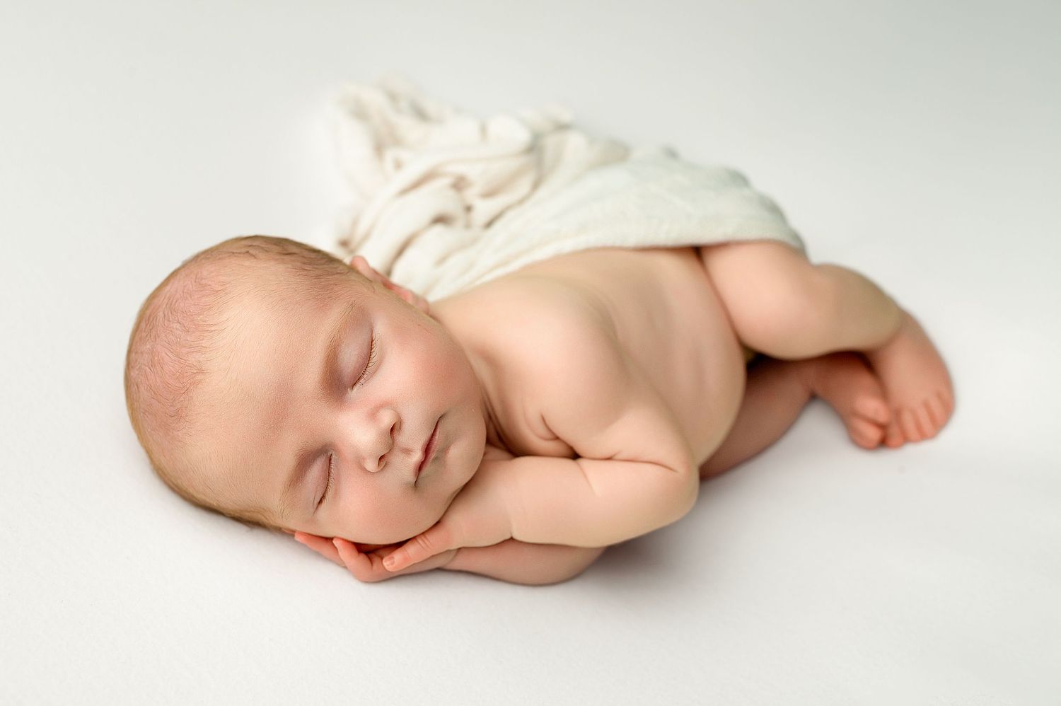 A peaceful sleeping newborn baby wrapped in soft white fabric lies on a light background.