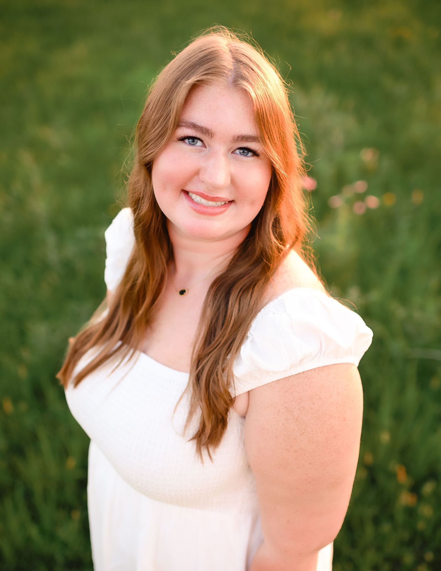 Summer portrait session in a green field wearing a white cap-sleeve top.