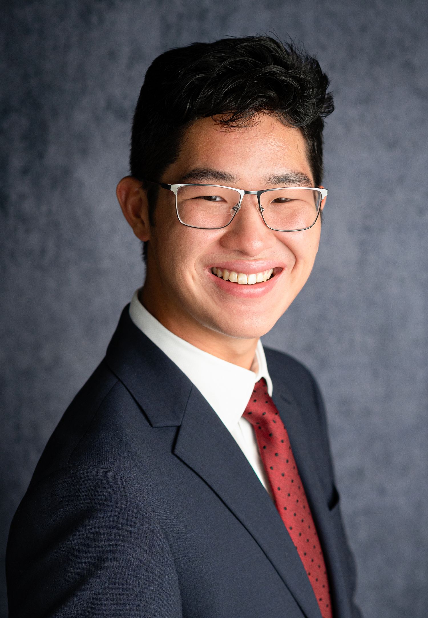 Professional headshots showing person in business suit and red tie against grey background.