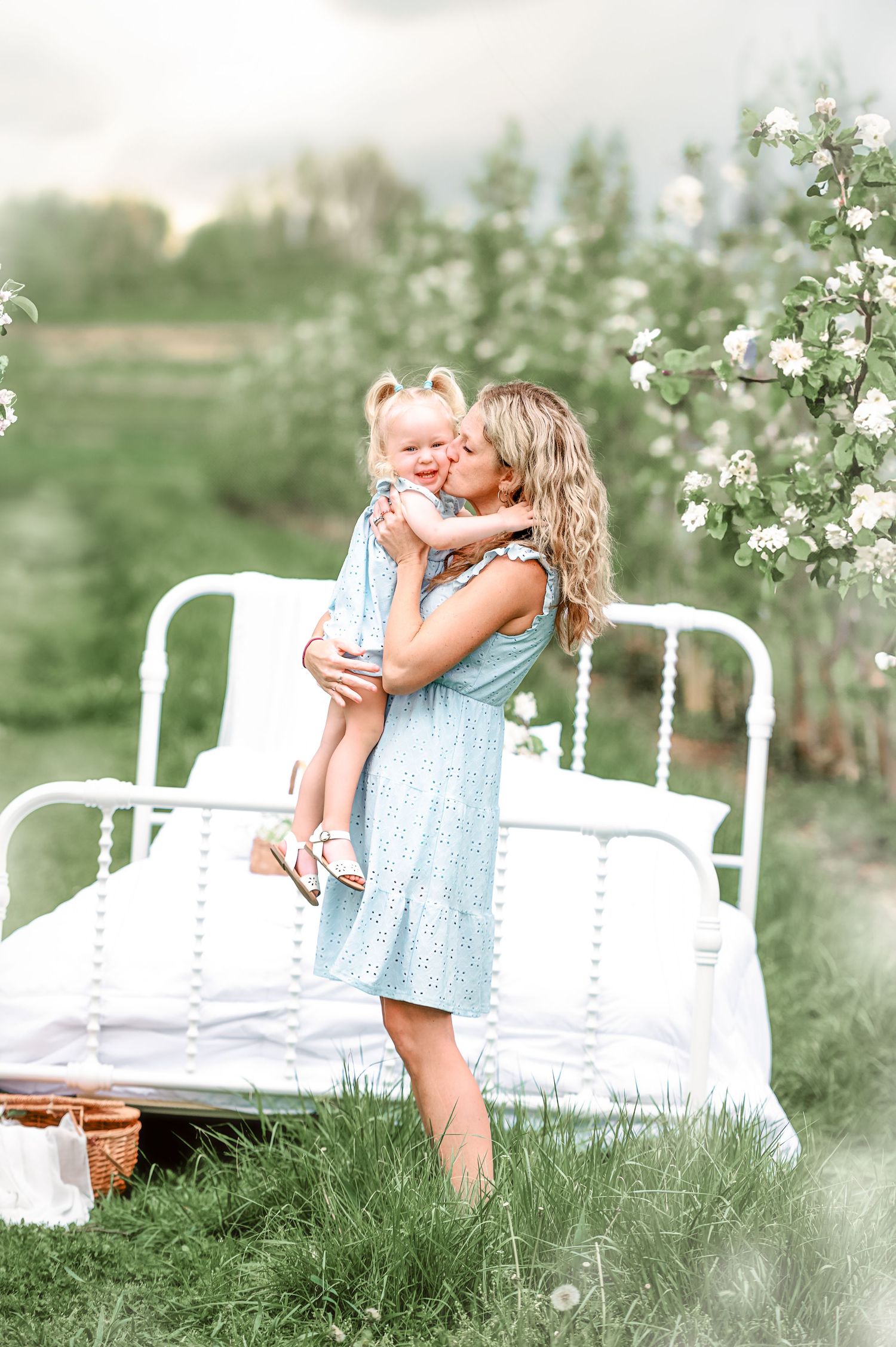 Sweet moment between parent and child on white iron bed in blooming orchard.