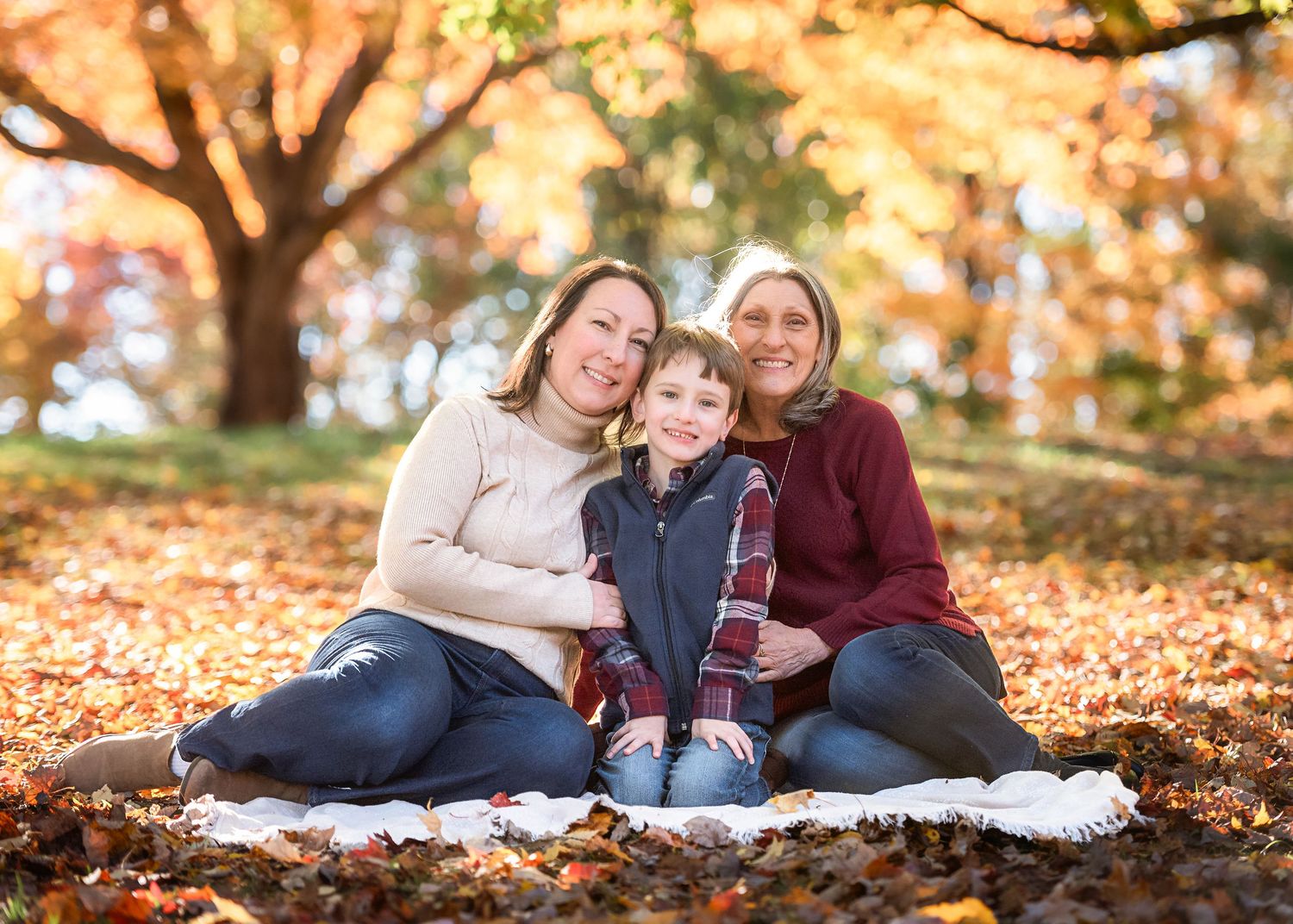 Family sits together on blanket surrounded by golden fall foliage.