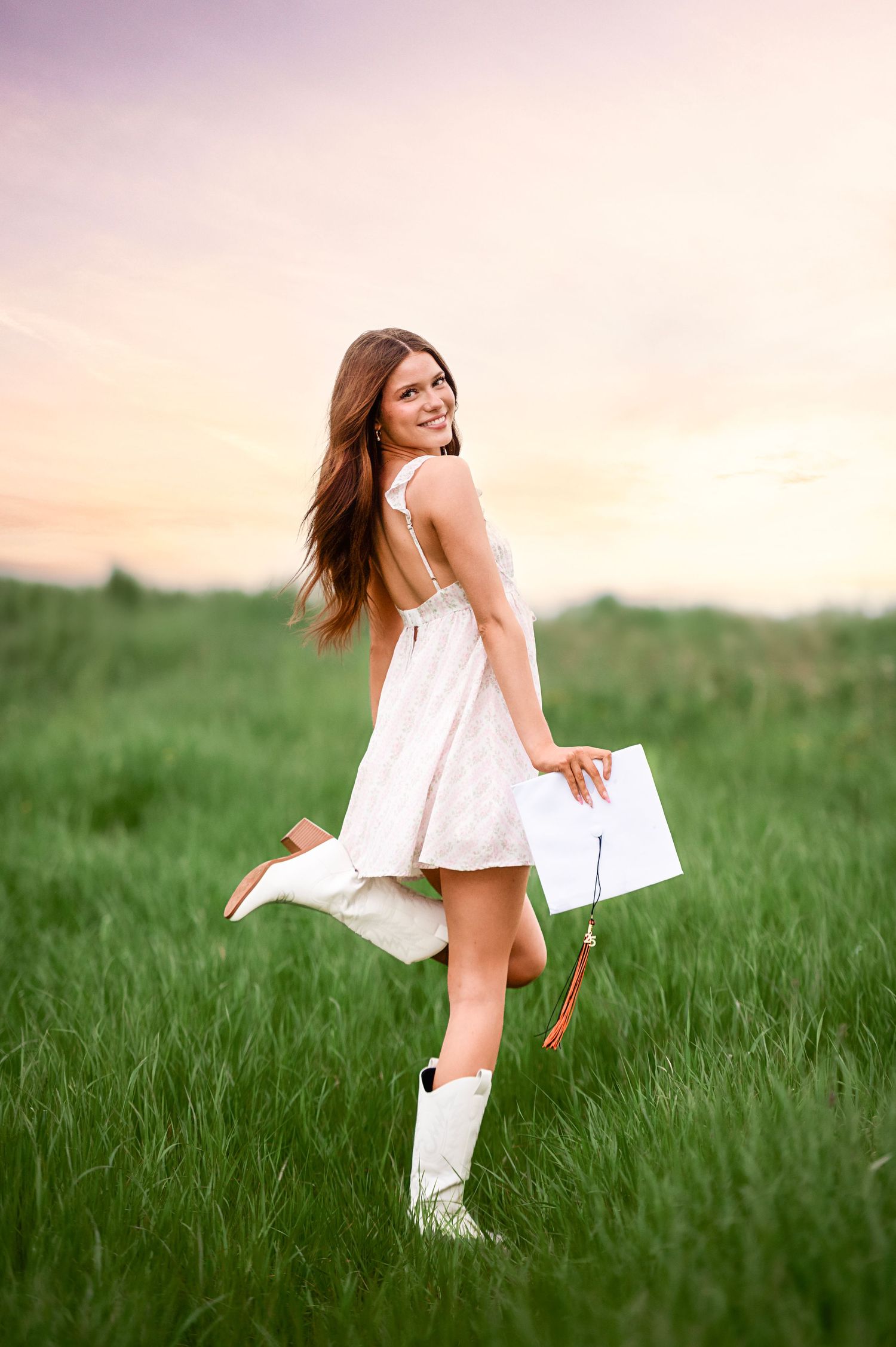 Woman in white sundress and boots twirls in grassy field at sunset.