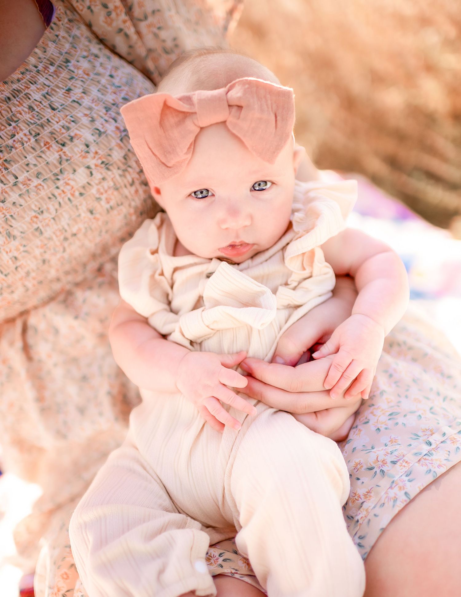 A baby in soft pink clothing lying on floral patterned fabric in a series of gentle poses.