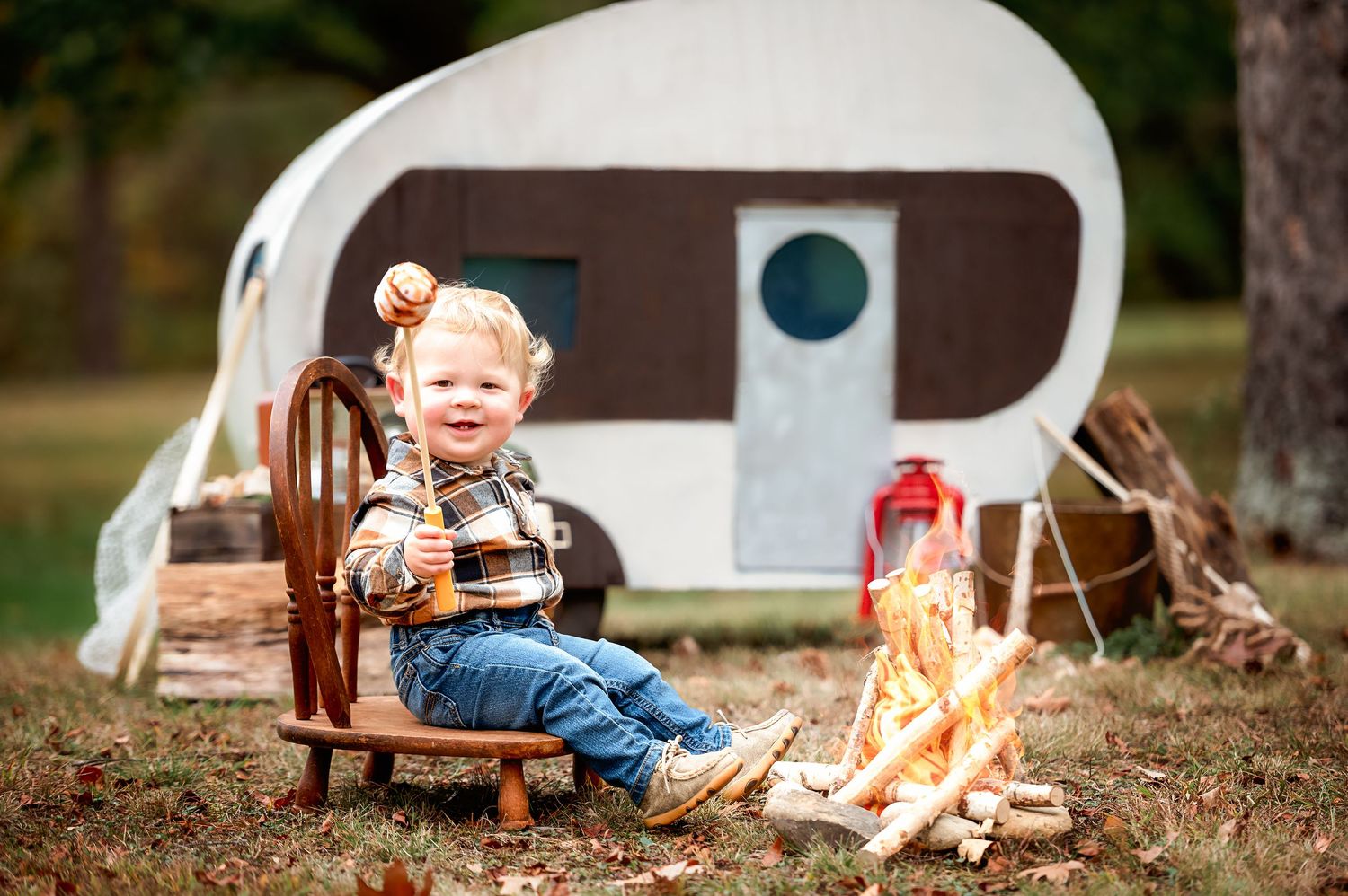 Rustic outdoor photoshoot setup with wooden props, blankets, and a glowing campfire in a natural setting.
