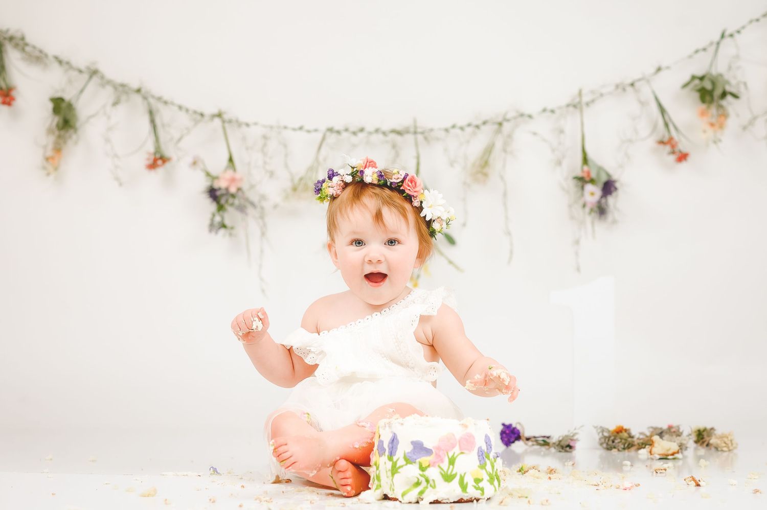 Baby with floral decorations and garland backdrop in soft lighting.
