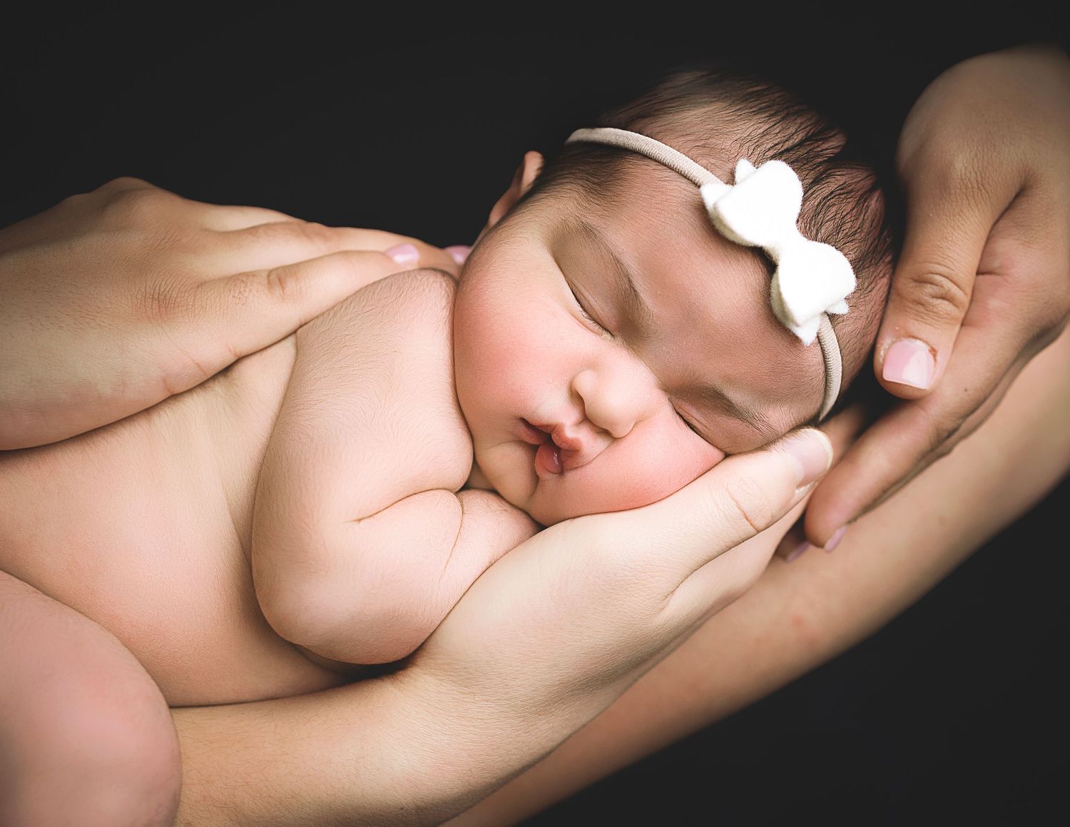 Artistic series showing sleeping newborn posed on dark background with dramatic lighting.