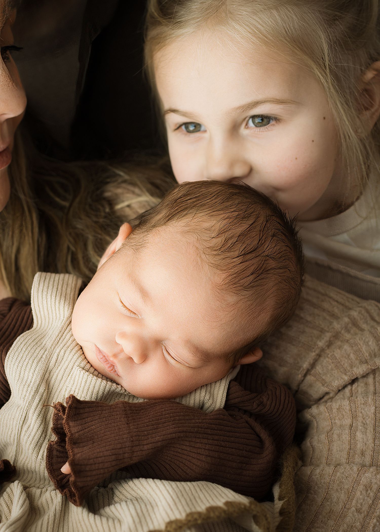 A sleeping baby in a brown corduroy outfit being watched by a child in a tender family moment.