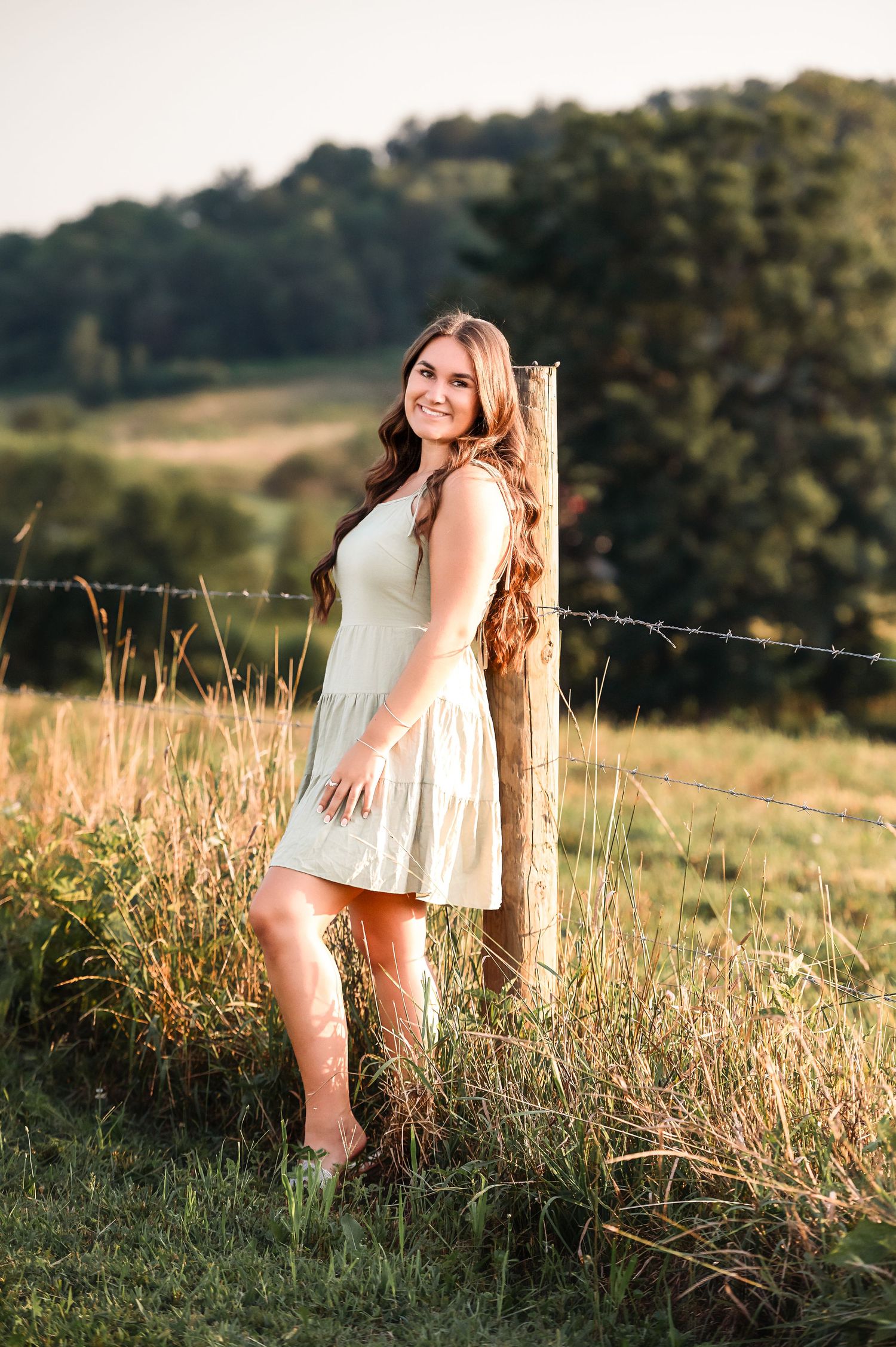 A summer portrait against a rustic fence post in a sunlit country field.