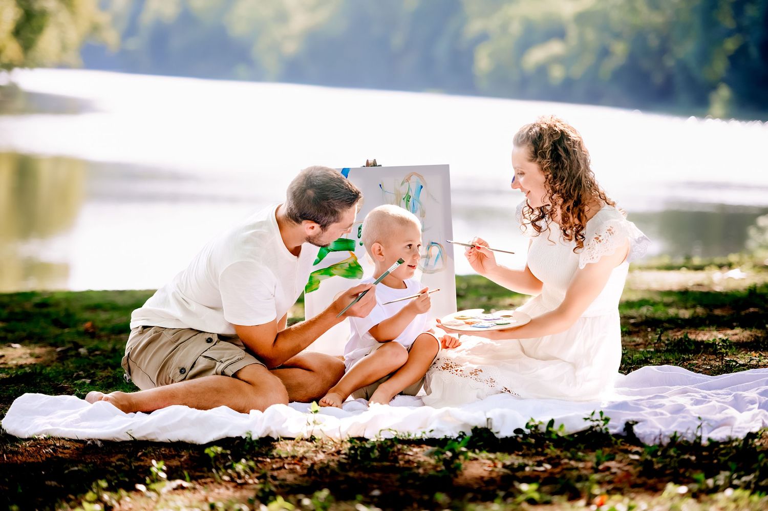 Family lying together on a white blanket in a sunny outdoor setting during a photo session.