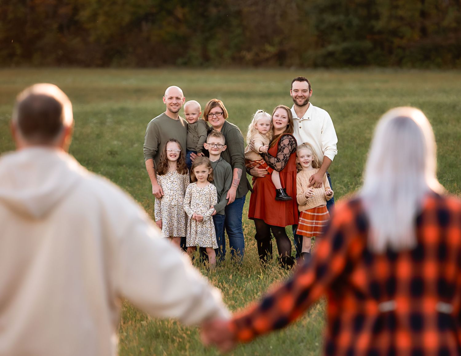 A group walks together through a grassy field at sunset wearing casual fall attire.