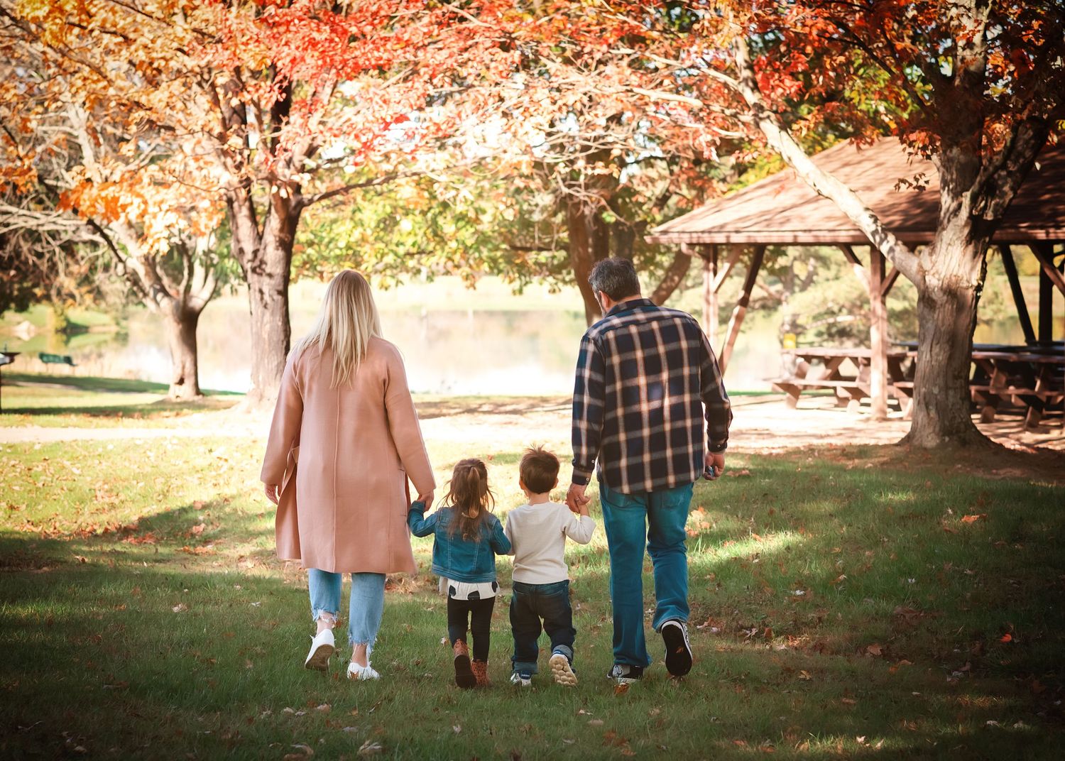A family walks together holding hands on an autumn path under golden trees.