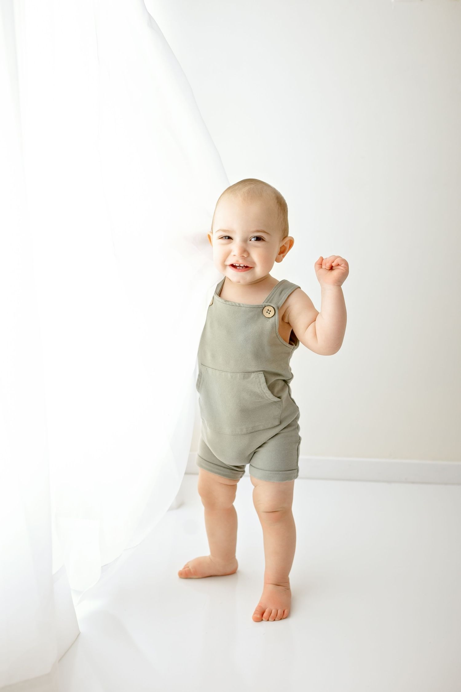 Baby in sage green romper standing against white background.