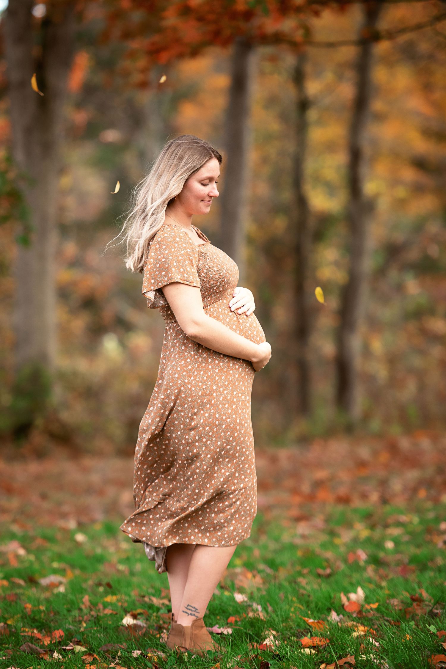 Maternity photos in polka dot dress amid autumn leaves and foliage.