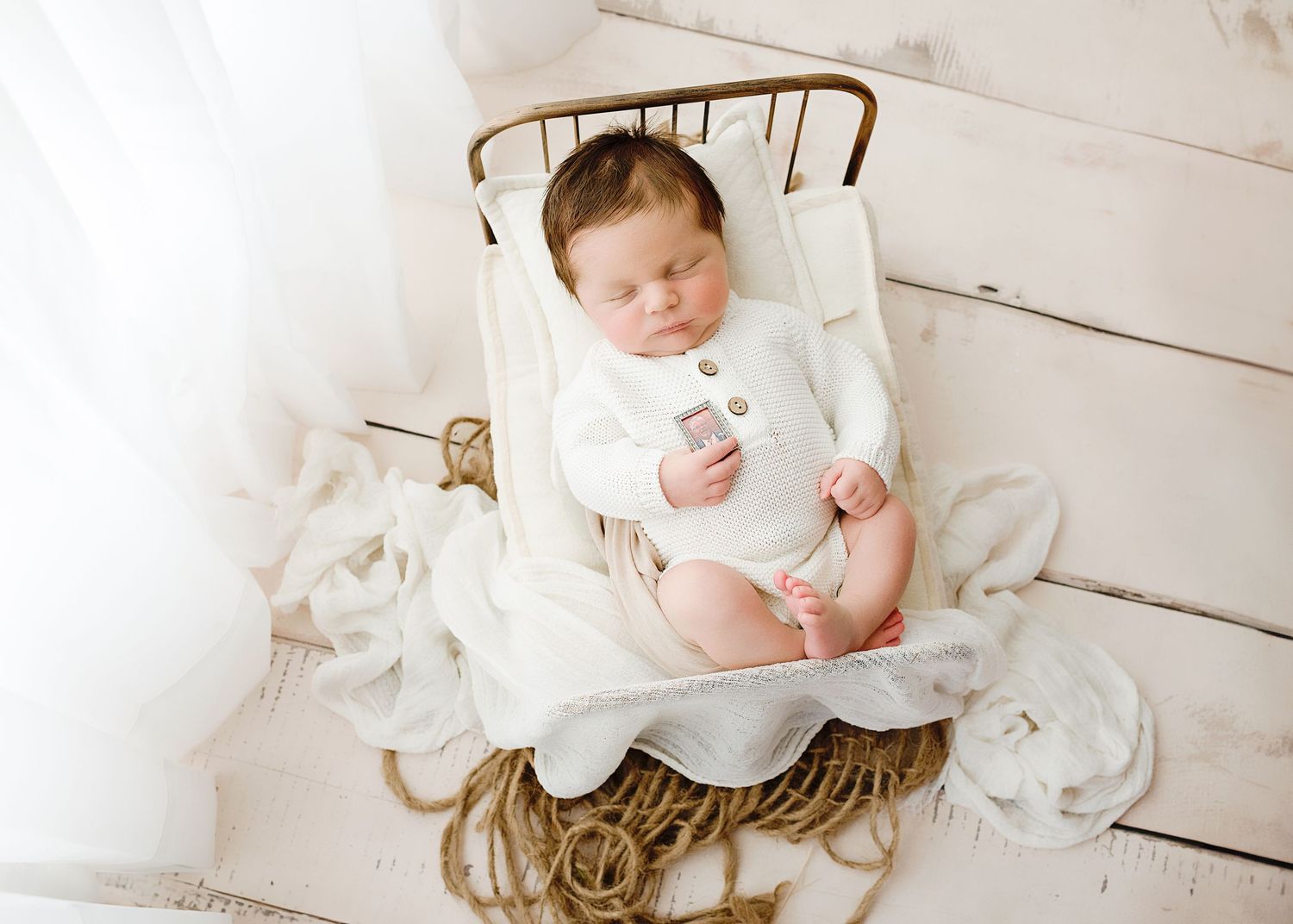 Newborn baby sleeping on white wooden floor wearing delicate cream-colored outfit.