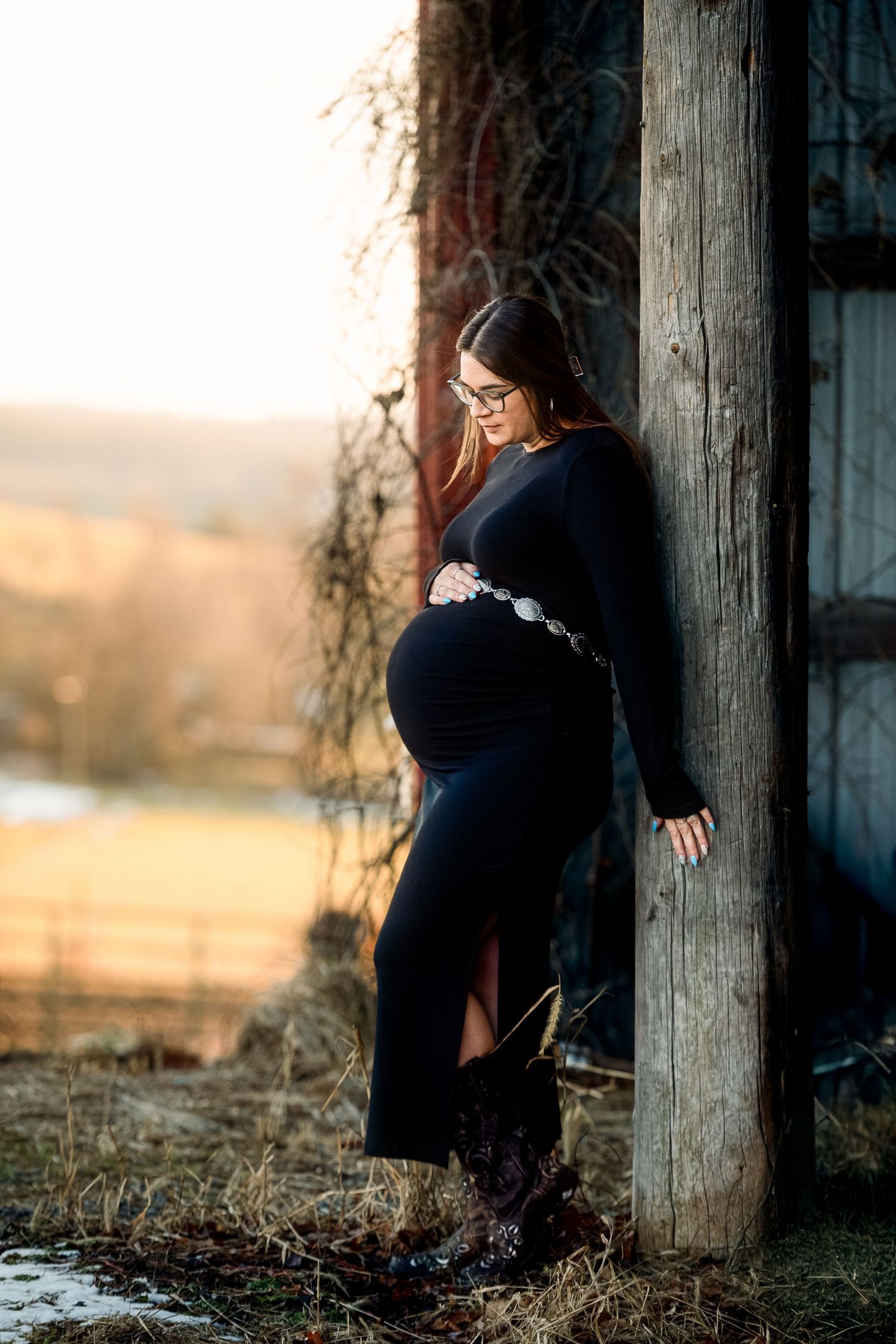 Silhouette of pregnant woman in black dress against rustic wooden backdrop.
