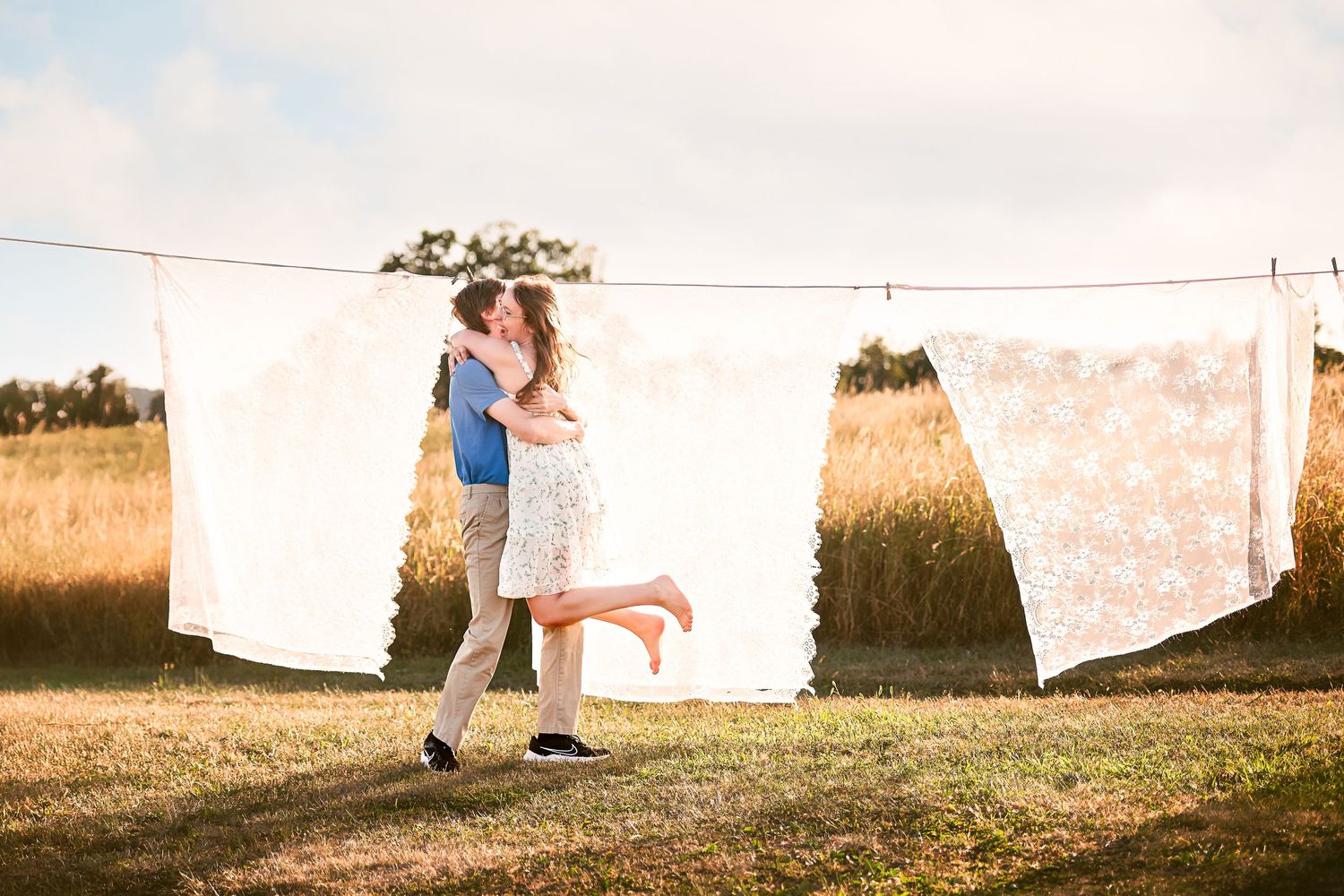 White sheets hanging on clothesline in golden field during sunset.