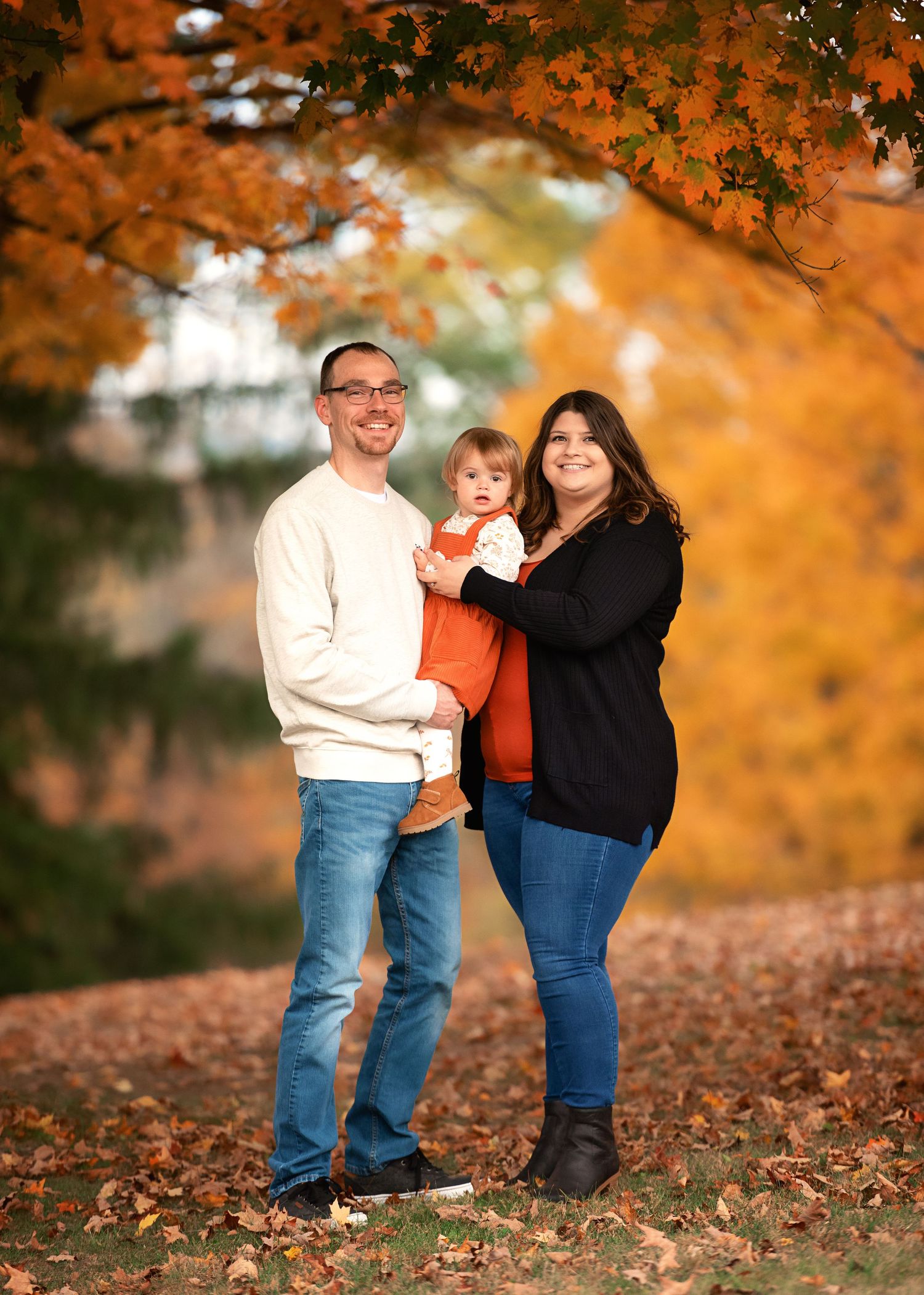 A family stands together under vibrant orange fall foliage.