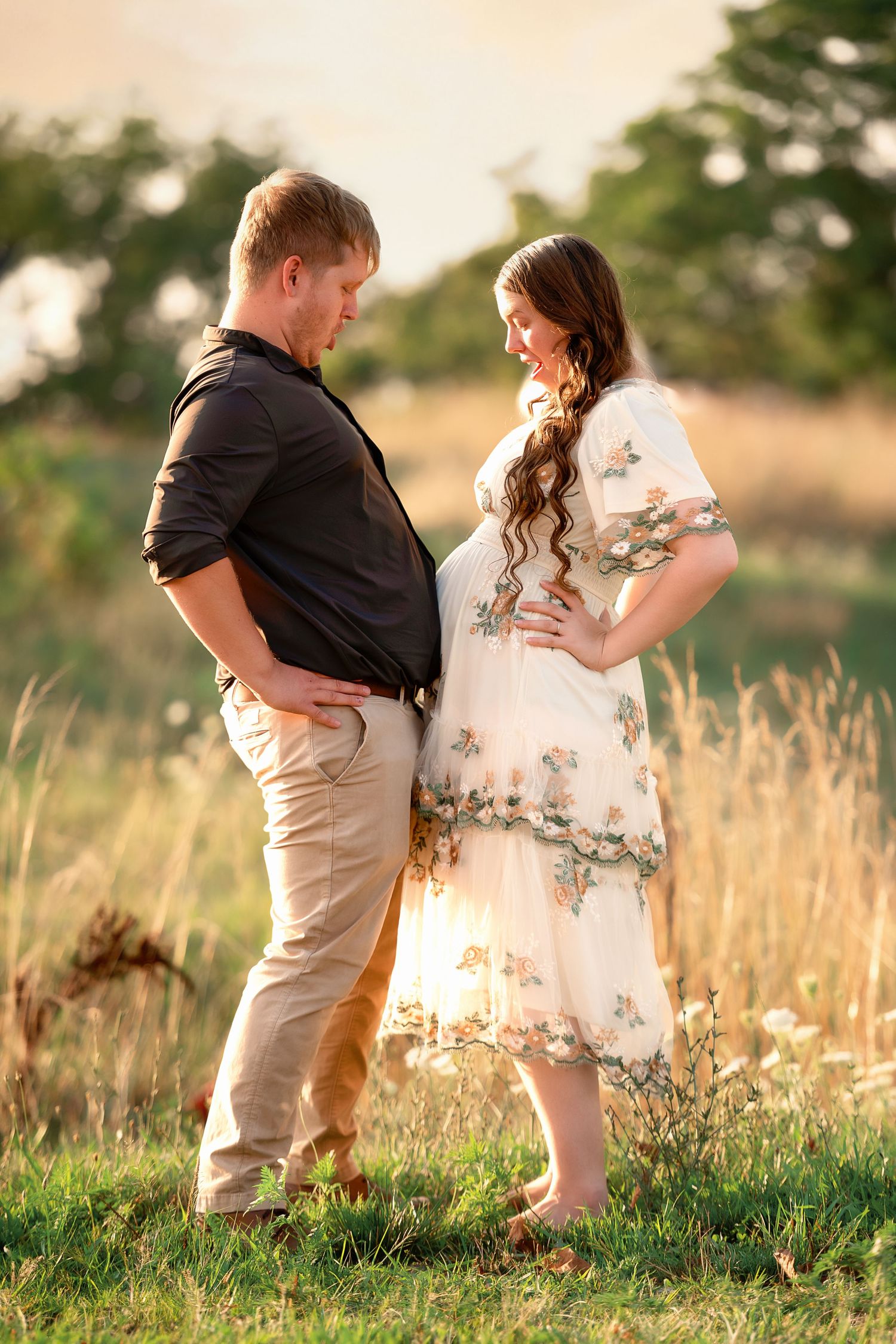 A romantic couple embraces in a sun-lit field of tall grass during golden hour.