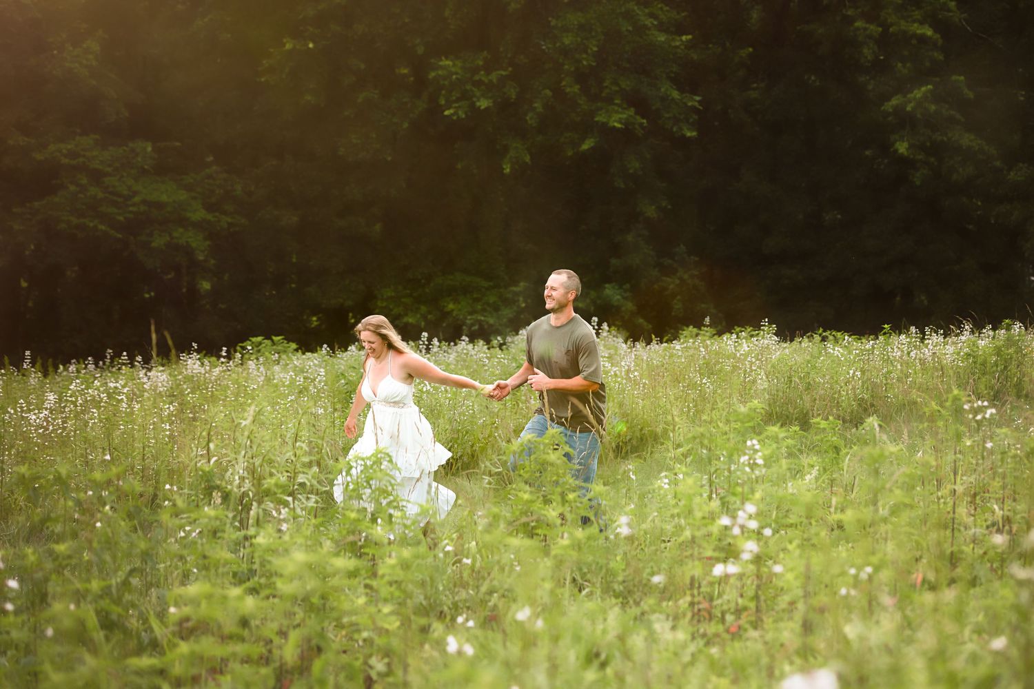 A couple enjoys a romantic picnic in a sunny wildflower meadow filled with white blooms.