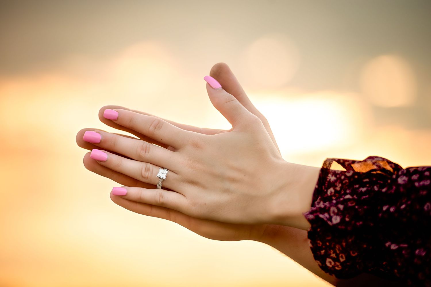 Hands displaying rings against a warm sunset sky background.