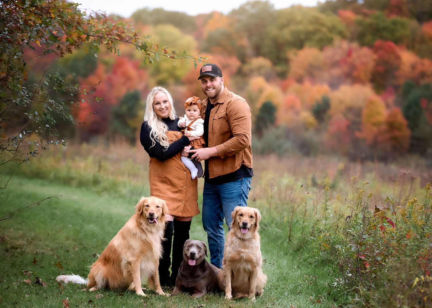 Family portrait with two golden retrievers against a backdrop of autumn colors.
