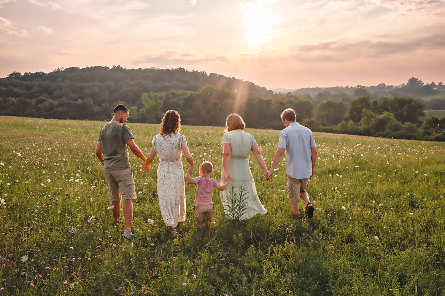 A group walks together through a sunlit meadow filled with wildflowers during golden hour.