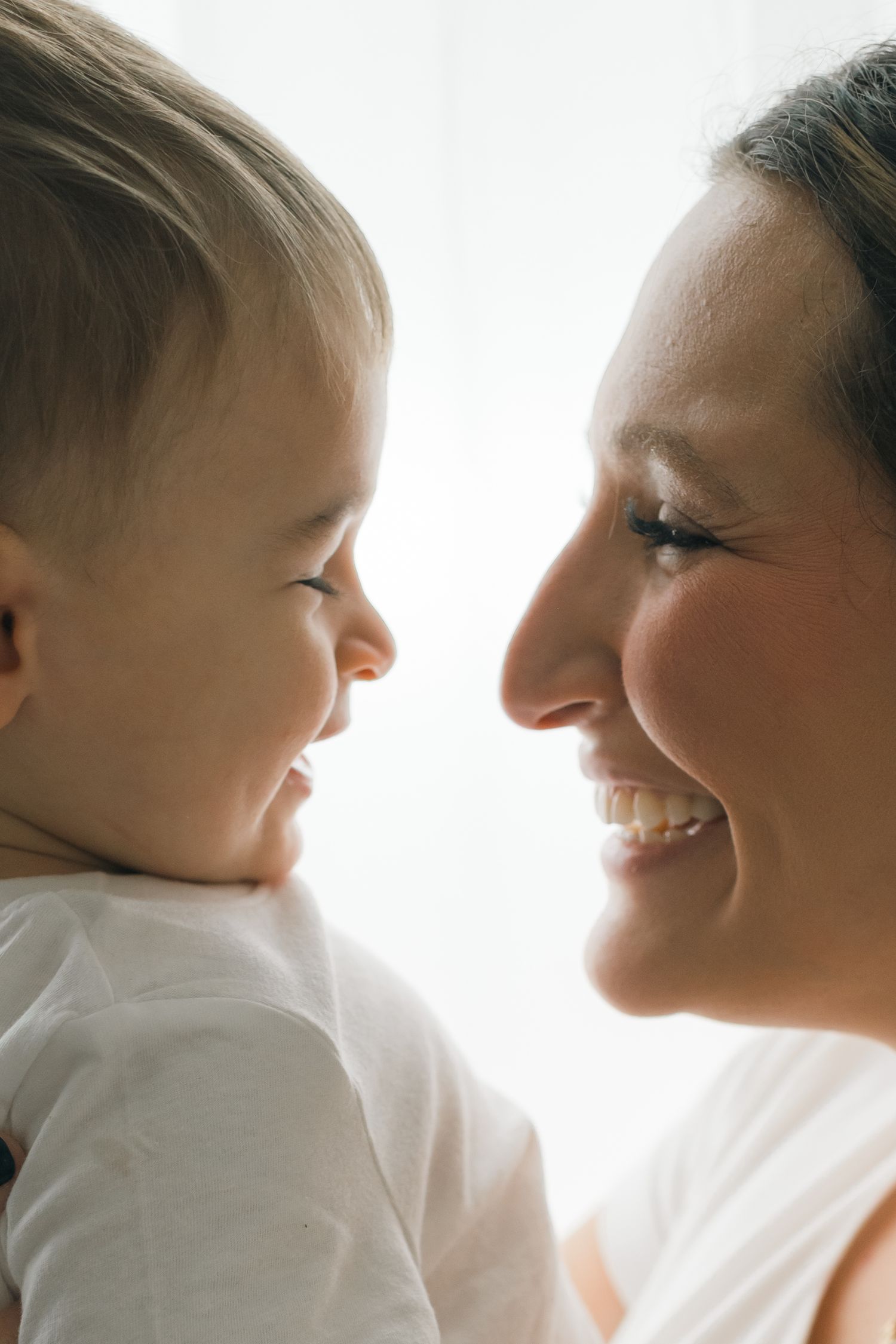 A tender moment captured in profile as parent and baby share loving glances in soft natural light.