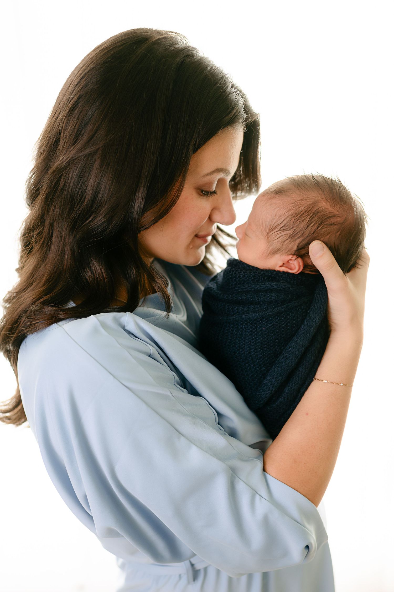 Parent in blue shirt holding and bonding with baby in white against bright background.